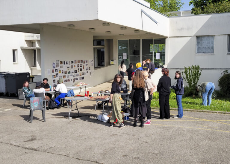 Devant l'ISBA, une dizaine d'élèves se rassemblent autour d'une table, les visages des participantes et participants sont floutés.