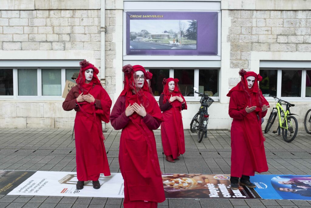 Sur le parvis de la mairie les "Red Rebelles" effectuent leur procession. Iels marchent sur un tapis du pubs deployé un peu plus tôt par des militant·es.