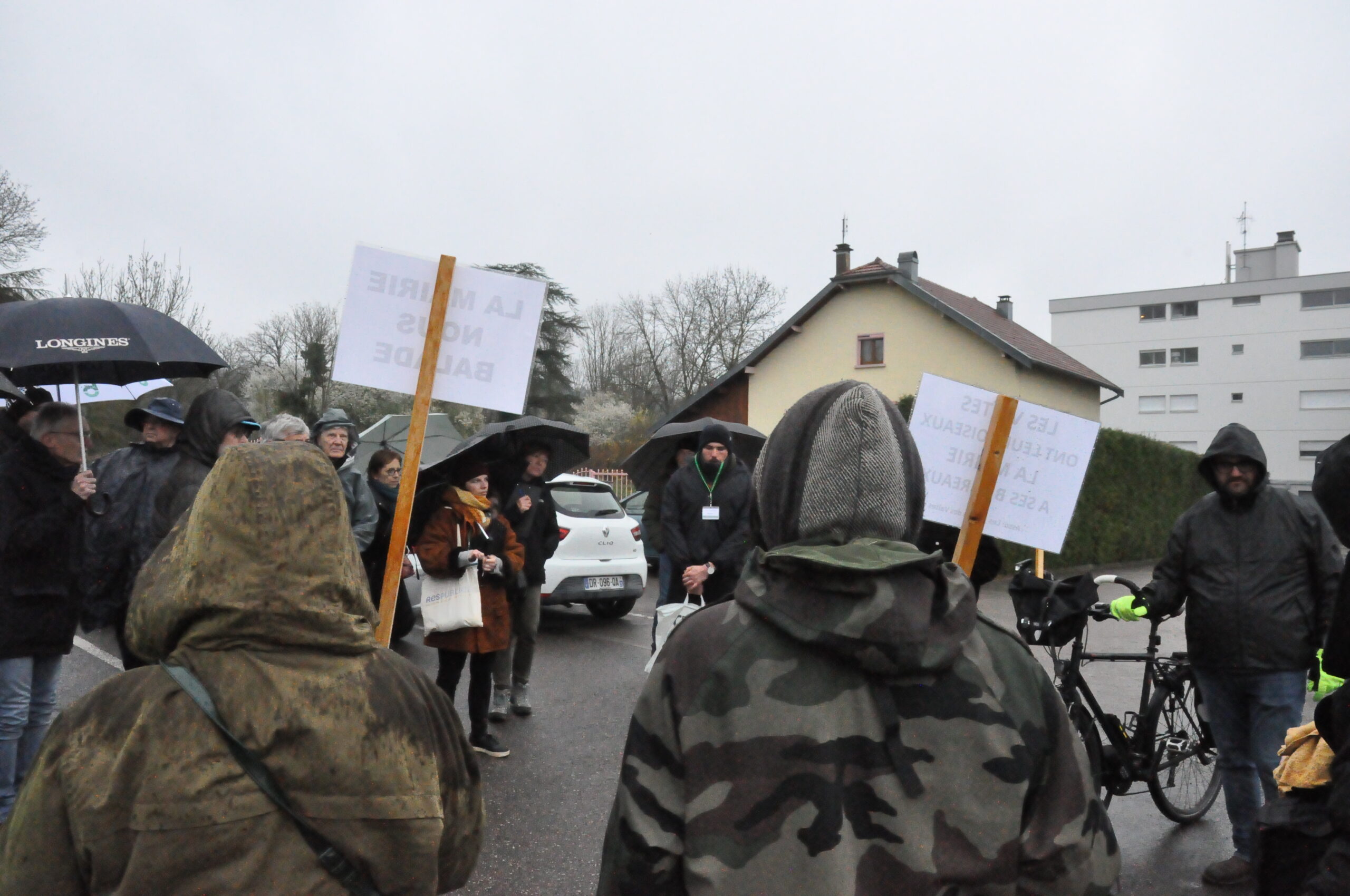 Rassemblement de manifestant·es sur le parking, brandissant des pancartes