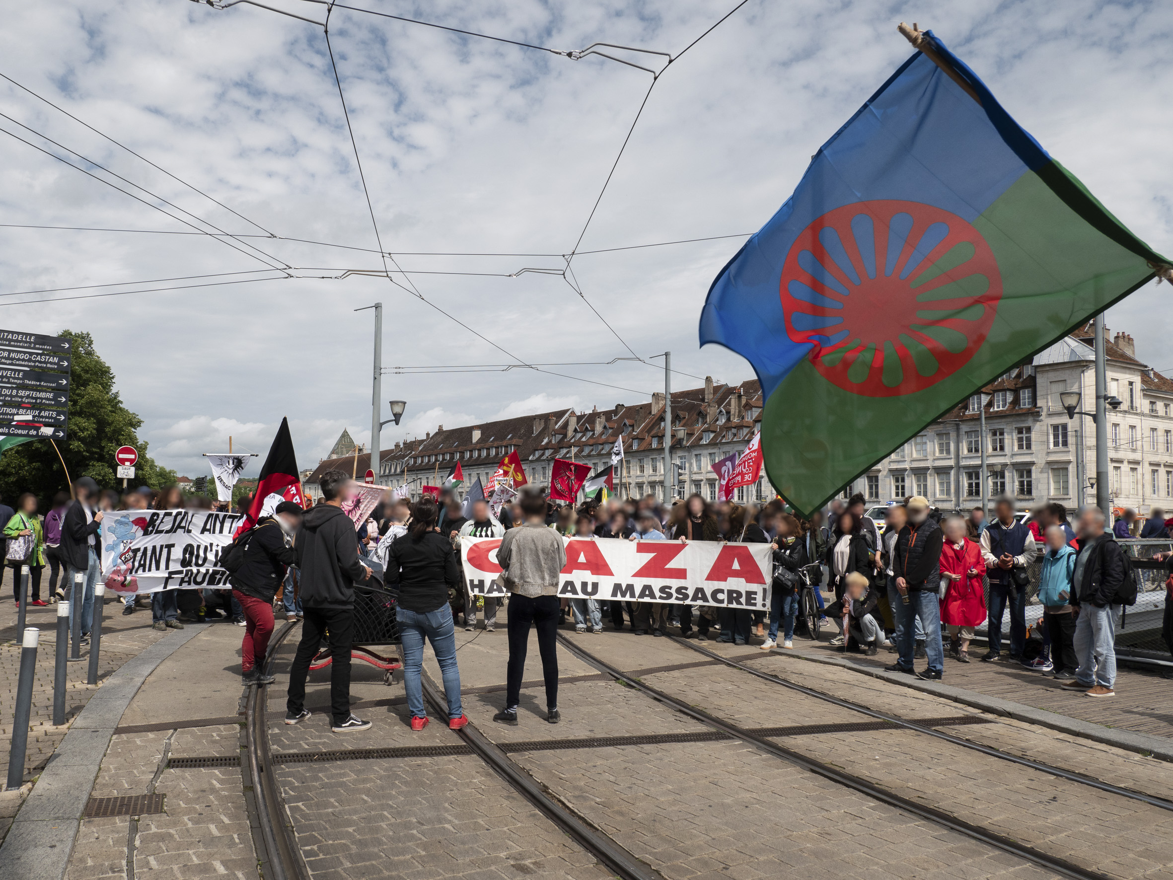 Le cortège arrêté au sortir du pont Battant, côté Madeleine, sur les rails du tram. À l'avant-plan, le drapeau des Gens du voyage