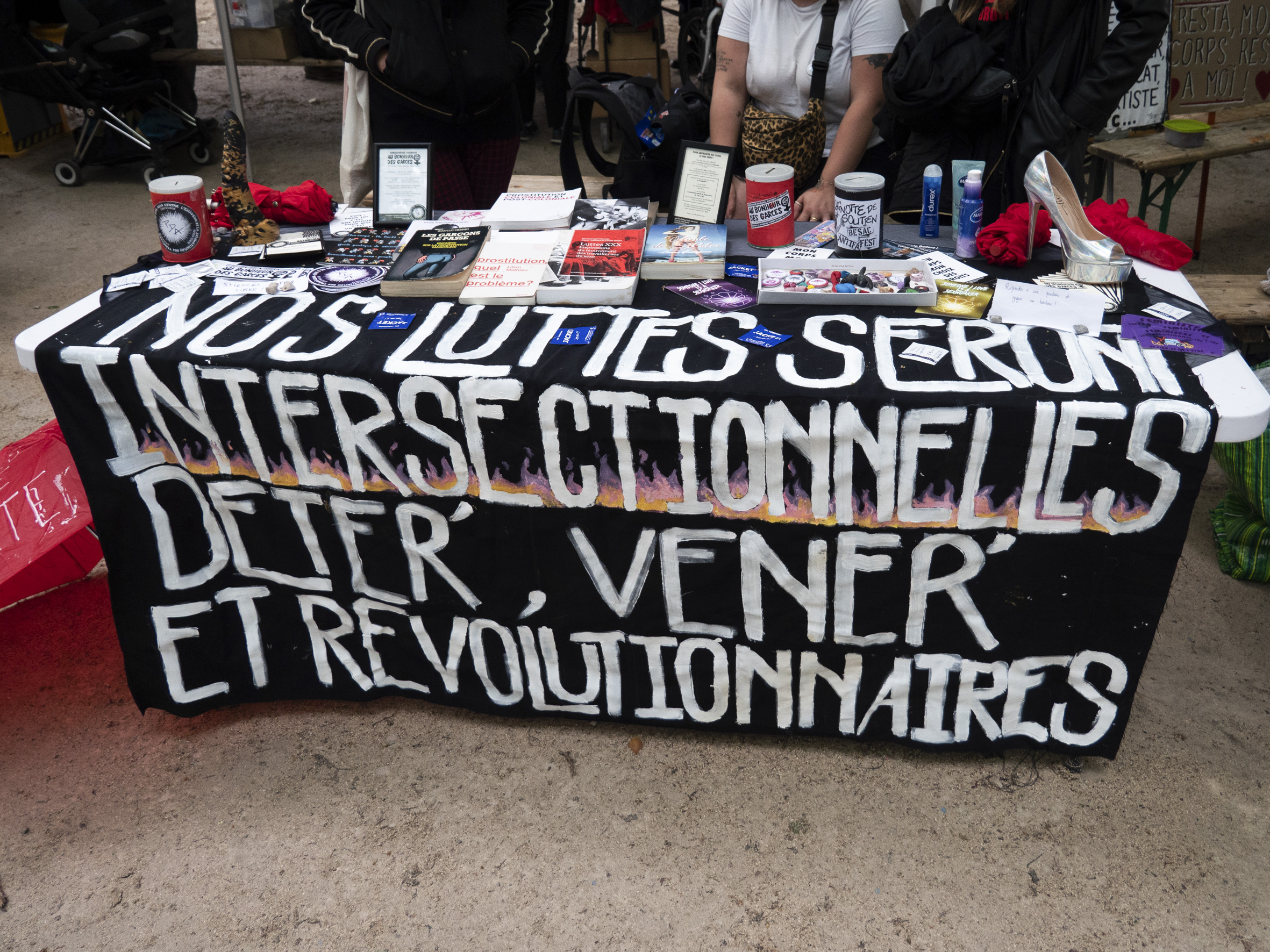 Une table d'articles et livres militants, posés sur un étendard "nos luttes seront intersectionnelles, déter', véner' et révolutionnaires