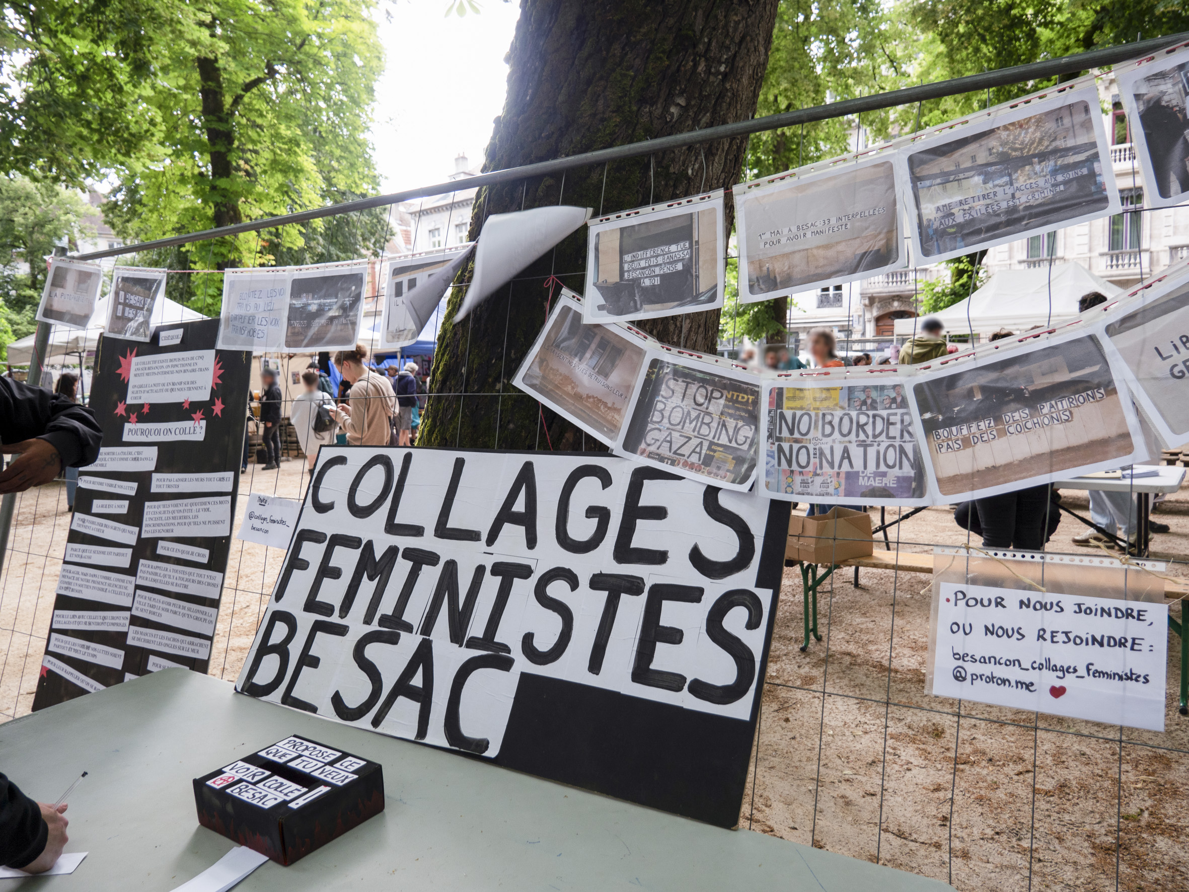 Vue du stand des collages féministes Besac, avec un ensemble de collages affichés sur une grille, contre un arbre
