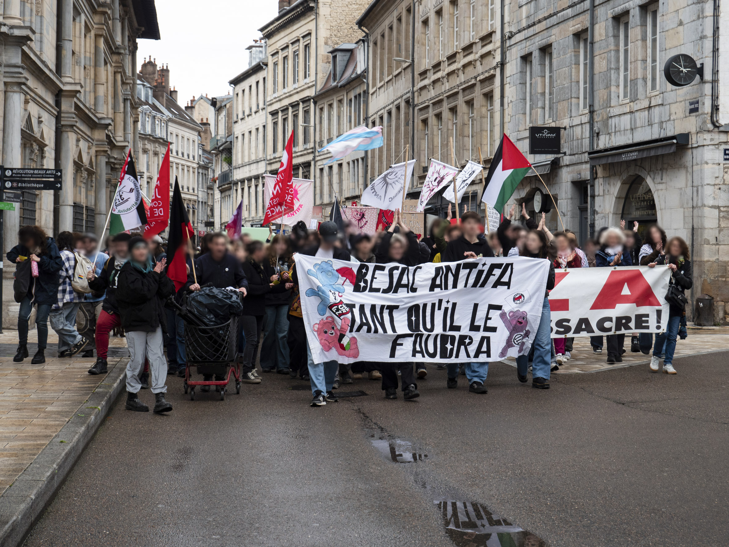Manifestation dans les rues de Besançon, avec en tête de cortège la banderole Besac Antifa tant qu'il faudra décorée de Bisounours.
De nombreux drapeaux sont visibles : palestinien, trans, communiste, anarchiste, antifasciste