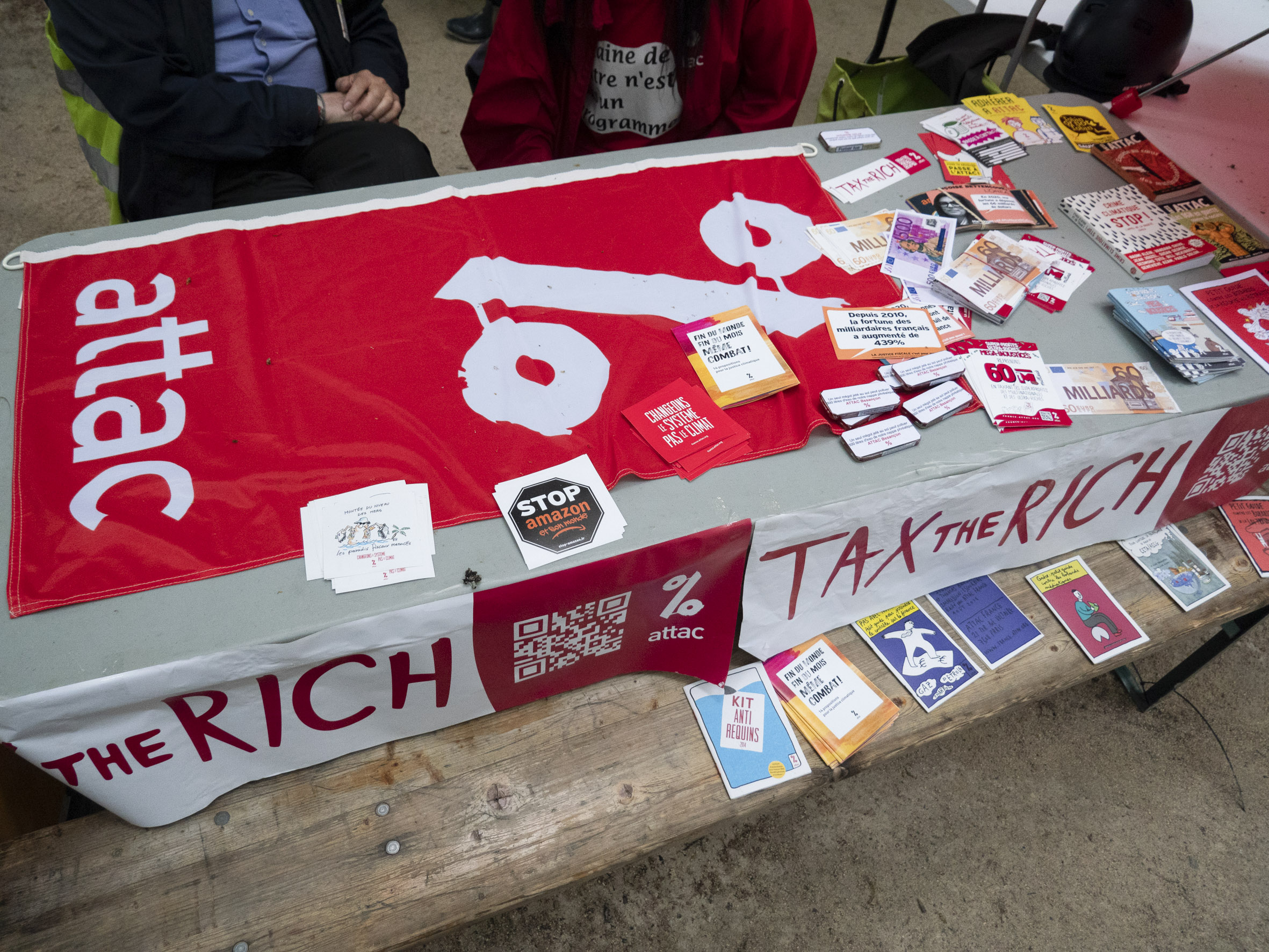 Le stand de Attac, avec divers ouvrages et stickers sur un nappe "tax the rich"