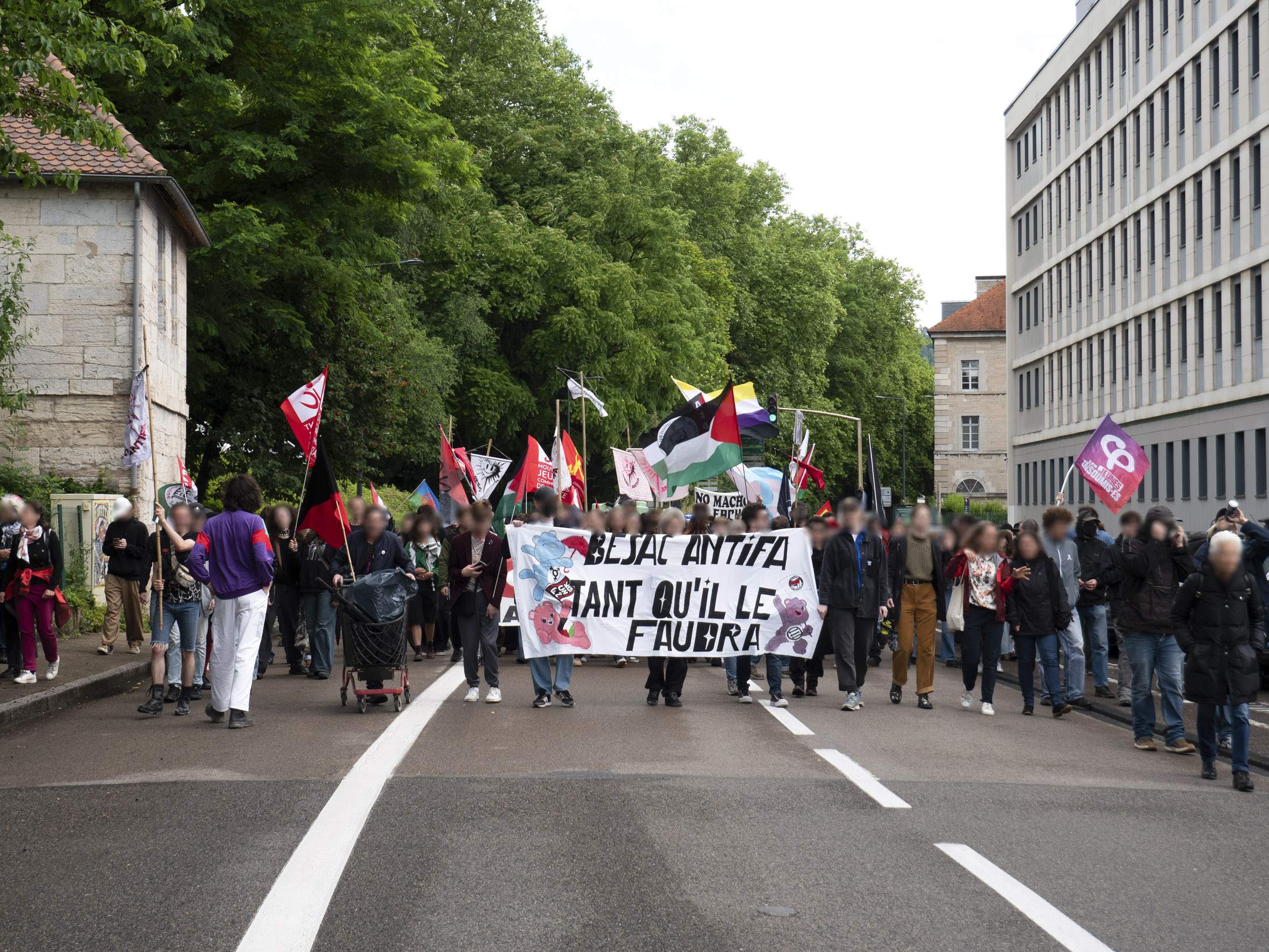 Manifestation dans les rues de Besançon (avenue Gaulard), avec en tête de cortège la banderole Besac Antifa tant qu'il faudra décorée de Bisounours.
De nombreux drapeaux sont visibles : palestinien, trans, communiste, anarchiste, antifasciste
