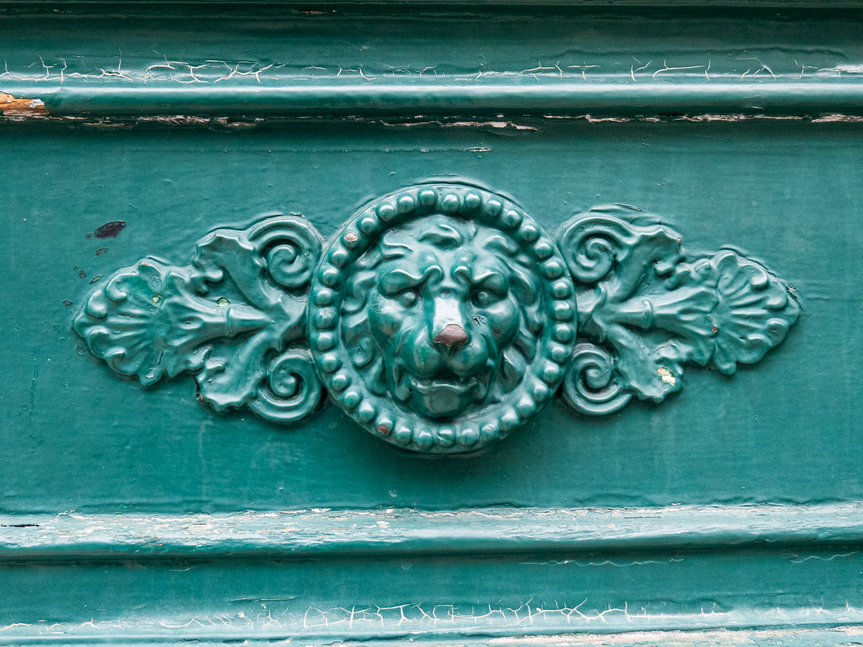 détails sculpté dans du bois d'une tête de lion dans un cercle perlé, flanqué de deux feuilles allant sur les côtés, le tout peint en vert