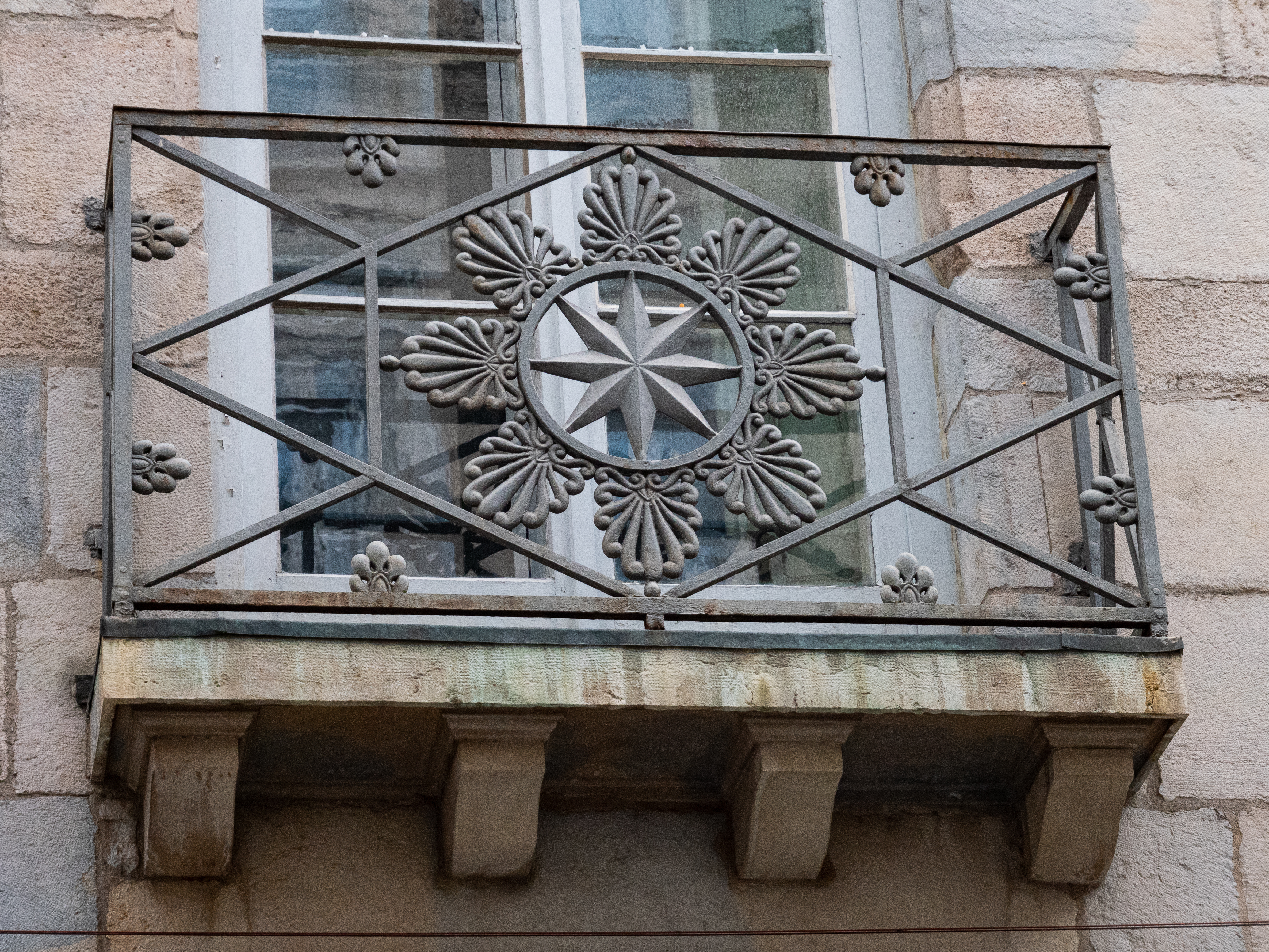 rambarde de balcon en fer, dessinant une étoile à 8 branches dans un cercle entouré de huit sculptures ressemblant à des bras de poulpes, le tour dans un losange relié aux coins de la rambarde