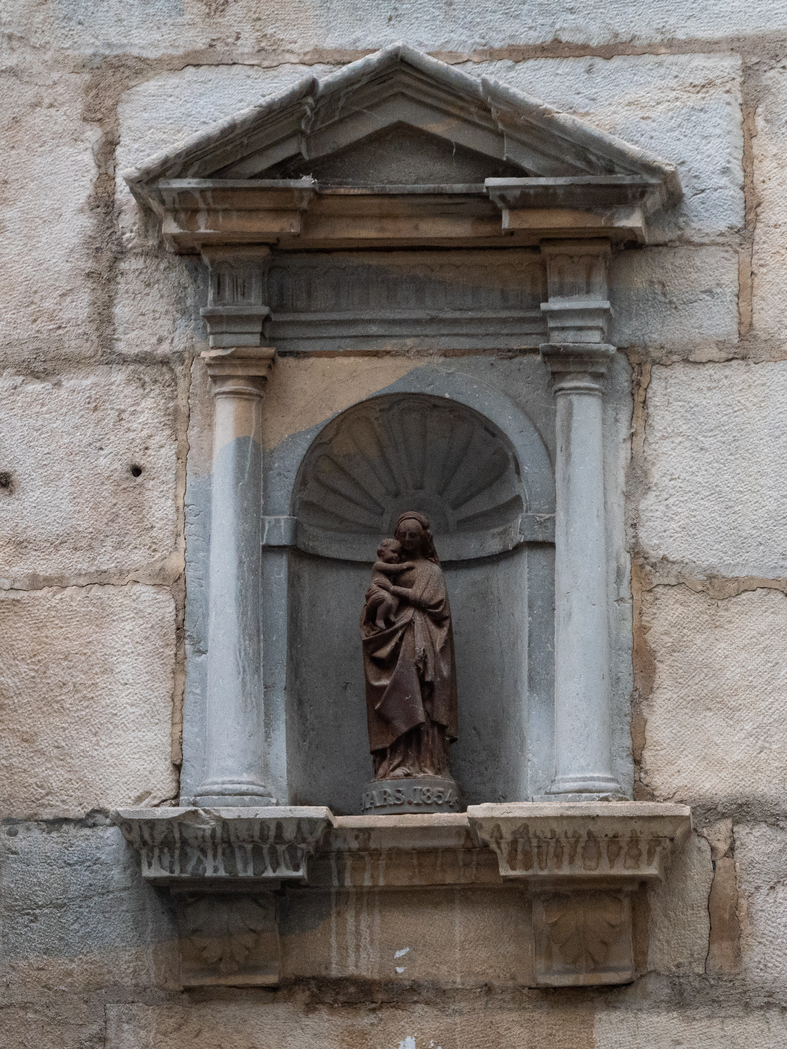 Sculpture en pierre de Marie tenant Jésus dans ses bras, dans un alcôve surmontée d'un fronton en triangle et flanqué de deux colonnes grecques