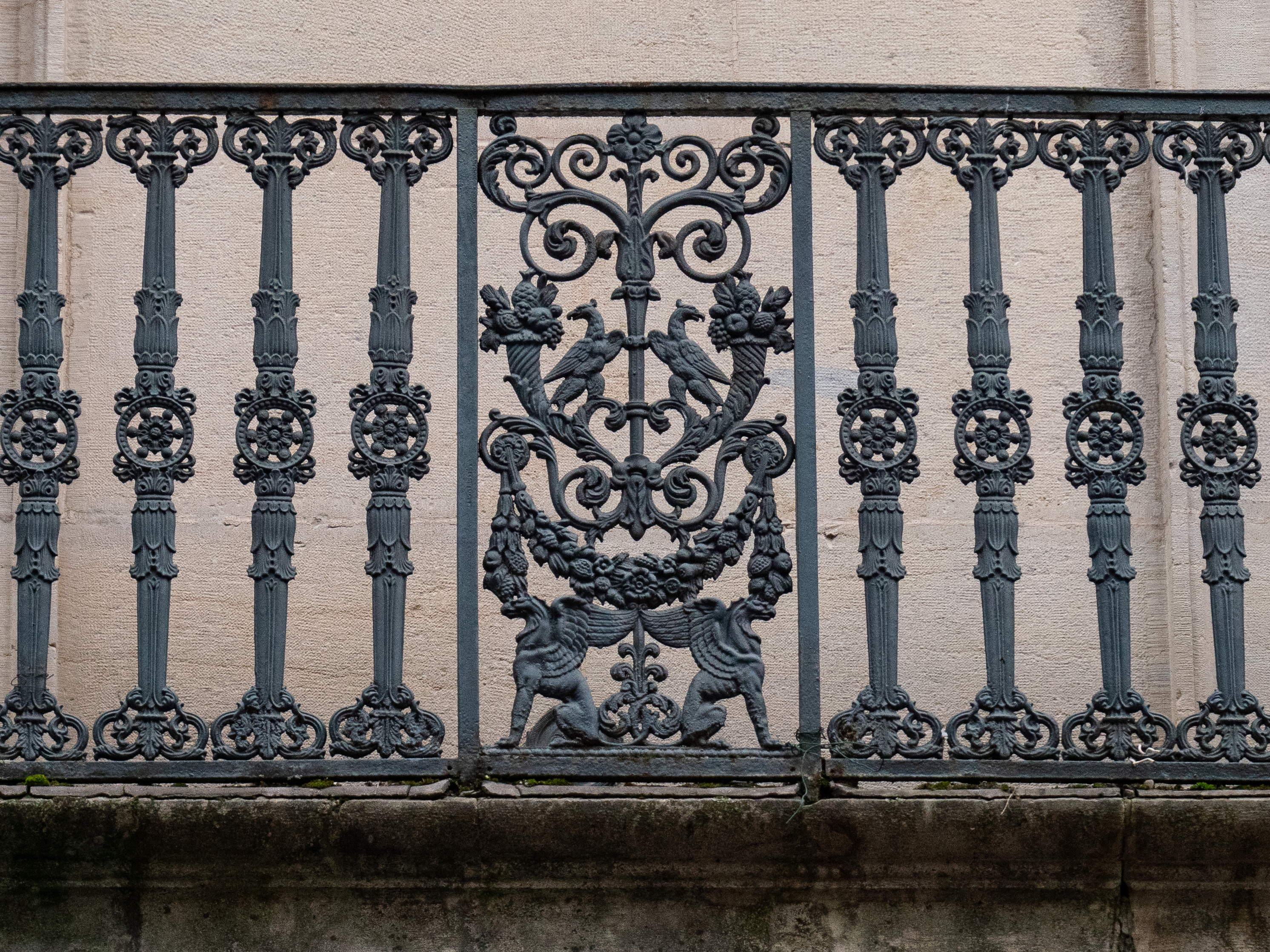 barrière en fer composée de barreaux sculptés de part et d'autre, avec au centre un assemblage de divers oiseaux et griffons symétriques, rattachés par quelques volutes 