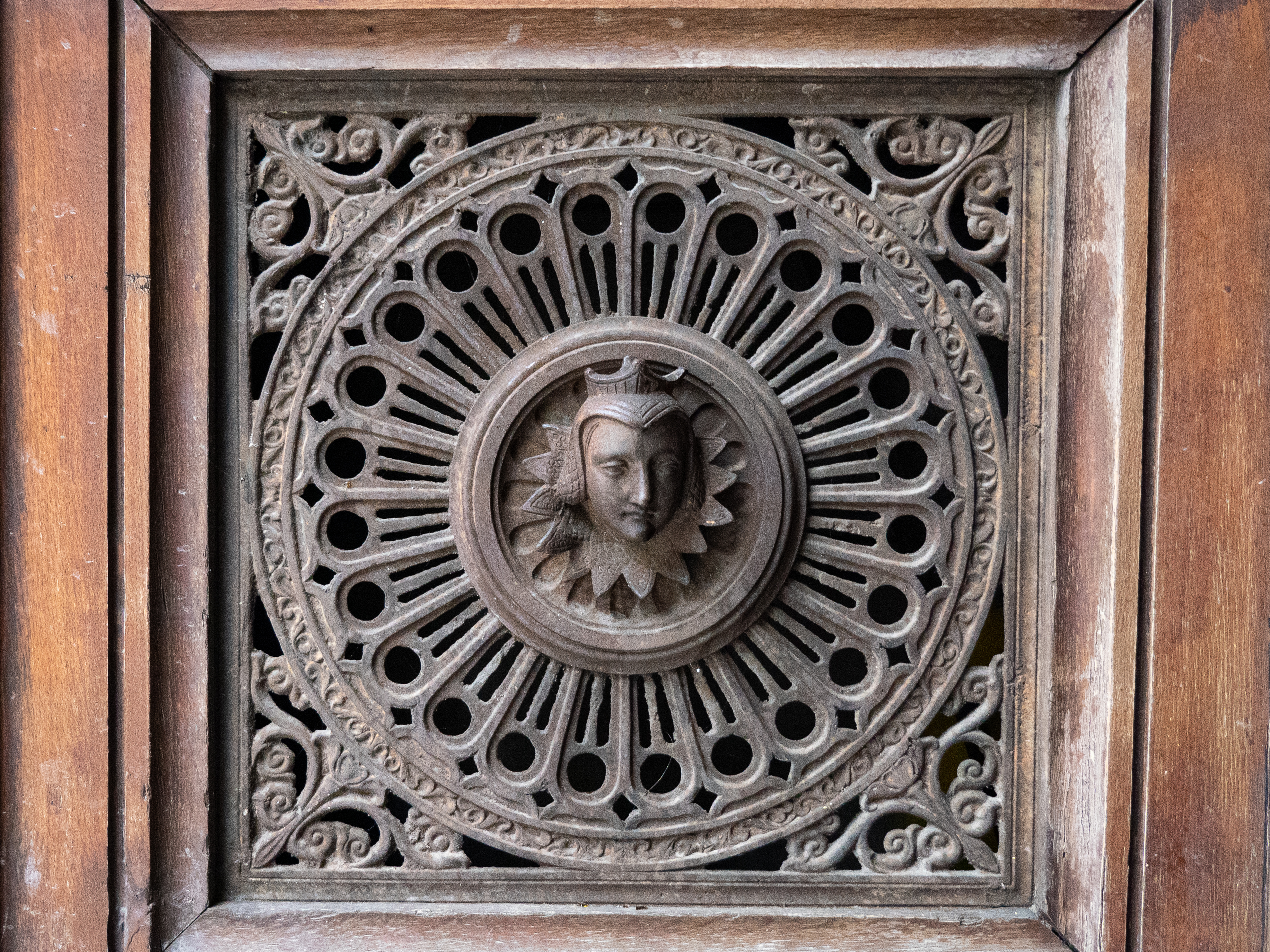 plaque de métal sculptée, insérée dans un mur en bois, représentant une tête d'homme dans un cercle lui-même entouré de motifs floraux dans les coins