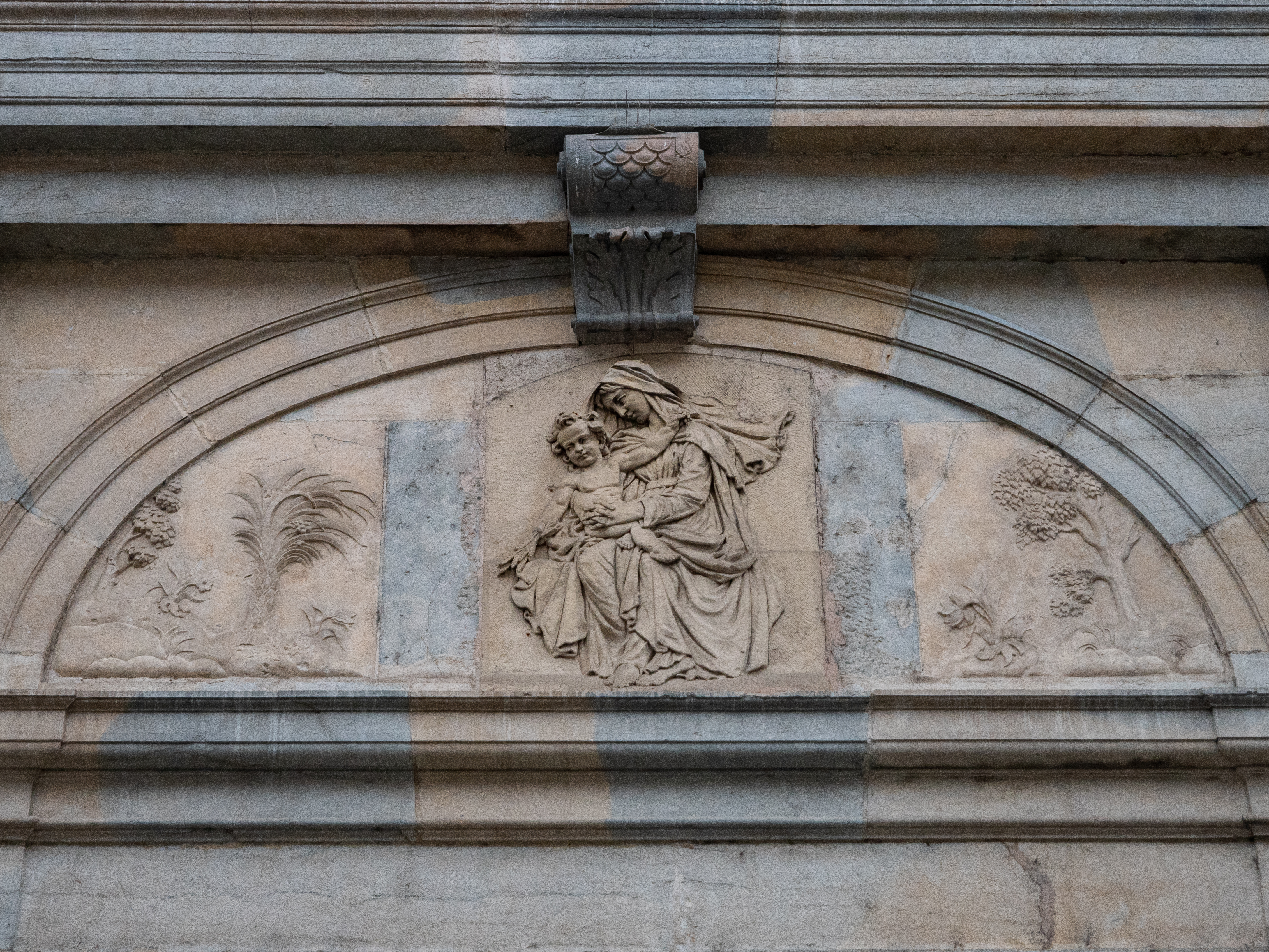 bas relief de Marie accroupie et Jésus dans ses bras, au fronton d'un bâtiment