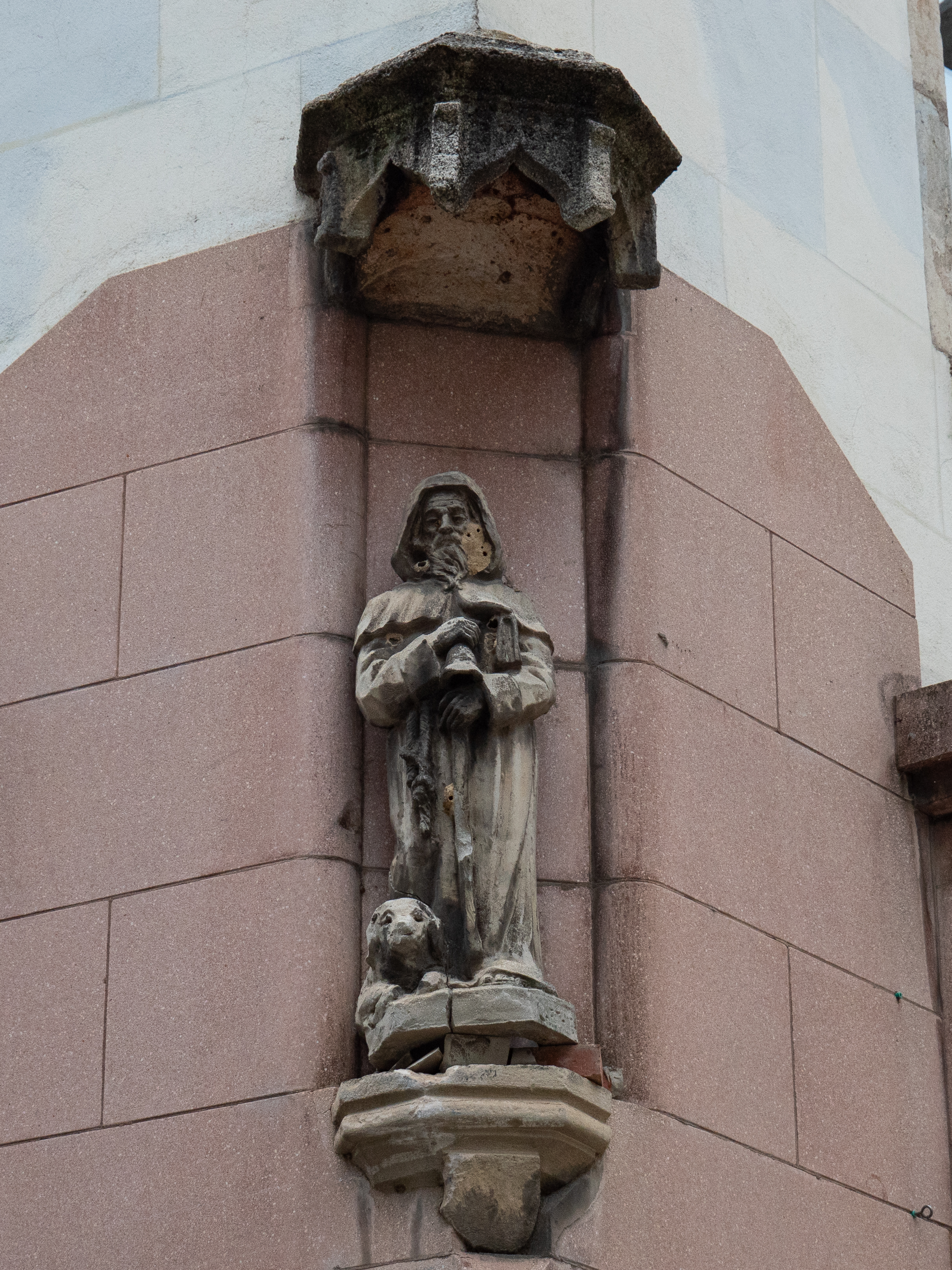 sculpture en pierre d'un sain à capuche, avec son chien à ses pieds, perché dans une alcôve 