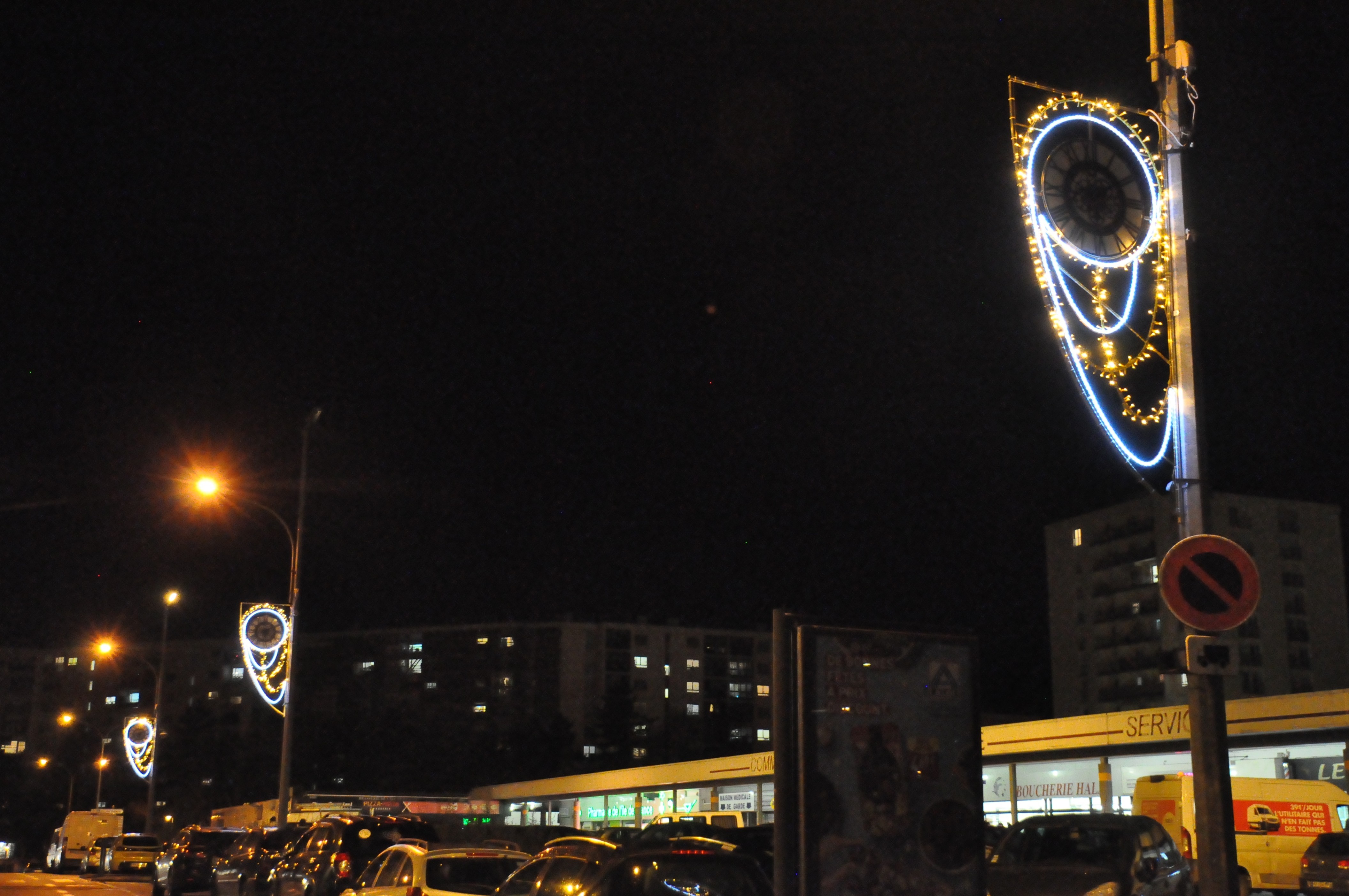 Trois illuminations posées sur des réverbères, représentant des horloges décorées. Les horloges ne sont pas éclairées.