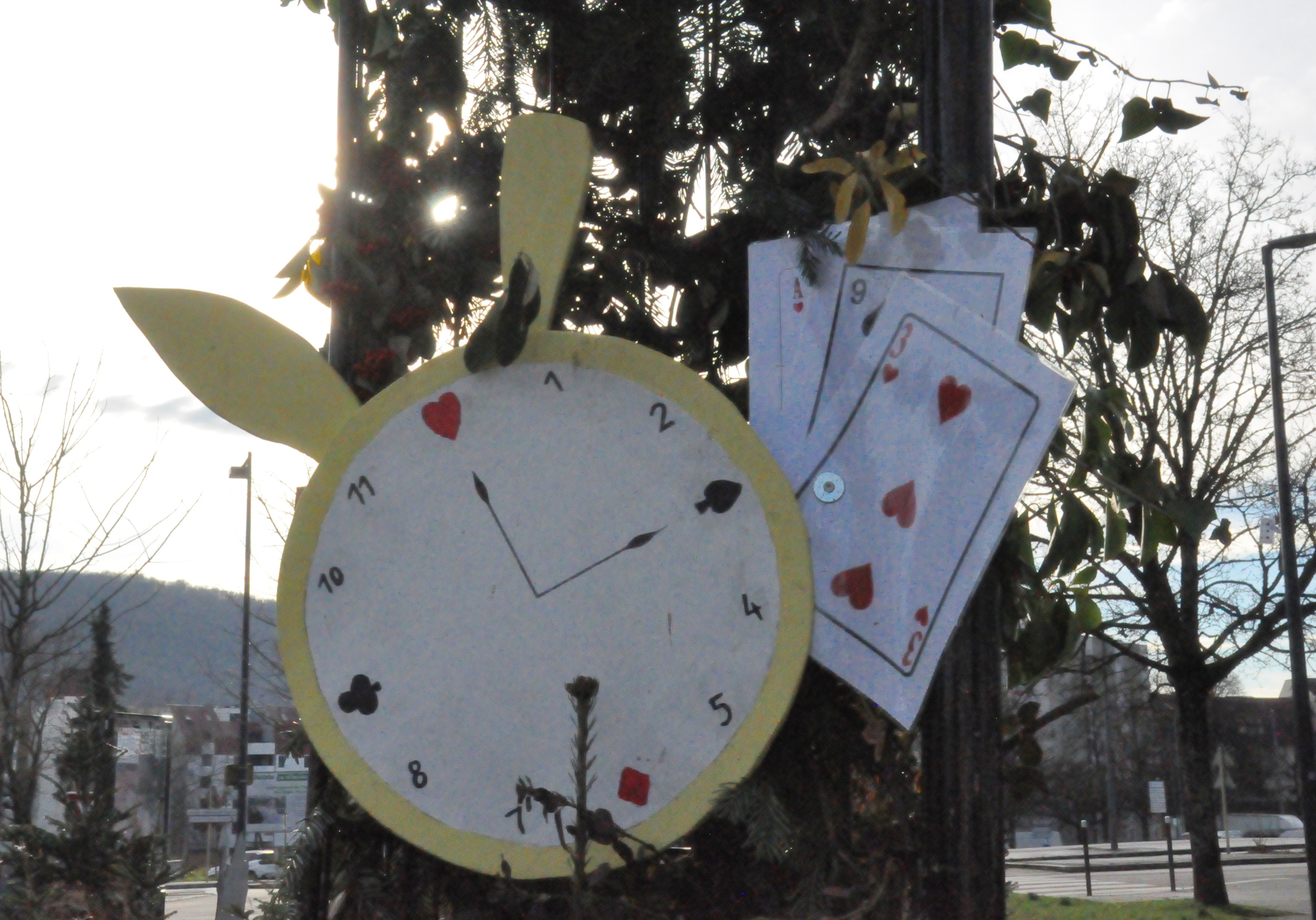 Photo d'une horloge avec des oreilles de lapin à côté de cartes à jouer, suspendues à des panneaux recouverts de branches.