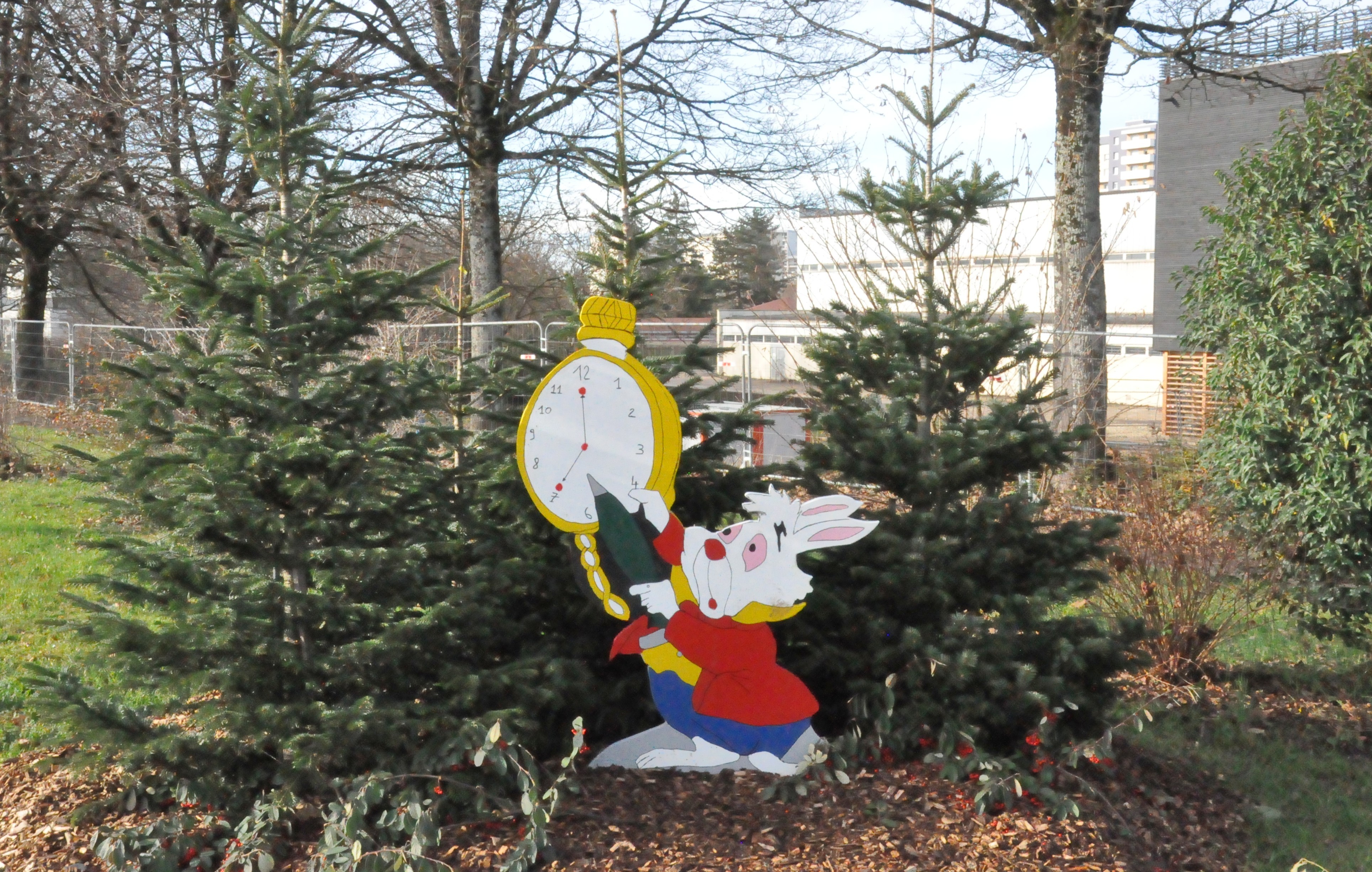 Photo de quelques petits sapins, au milieu desquels une effigie du lapin d'Alice au pays des merveilles a été plantée, avec sa grosse horloge à gousset et son parapluie.