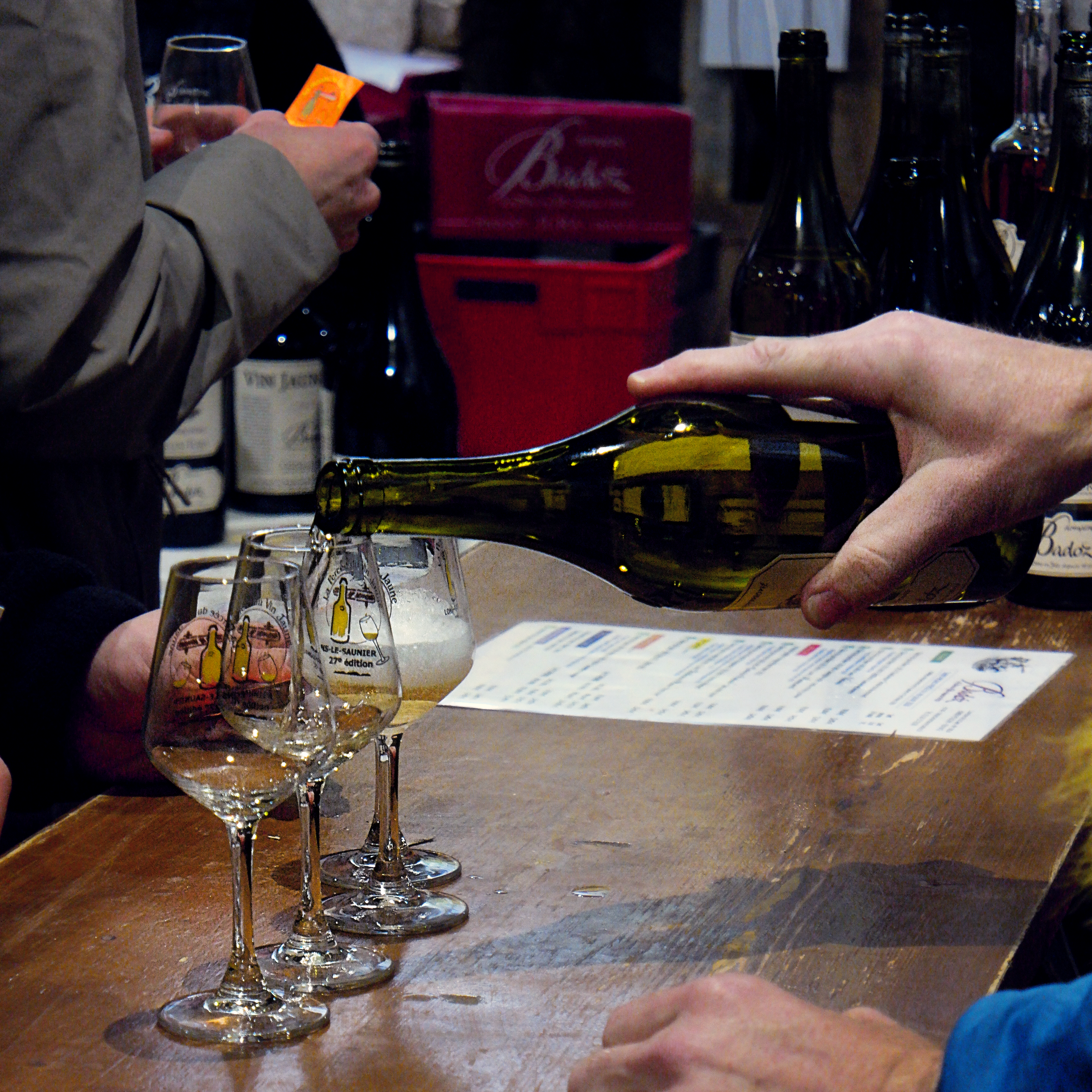 main en train de servir du vin jaune dans différents verres sur le comptoir
