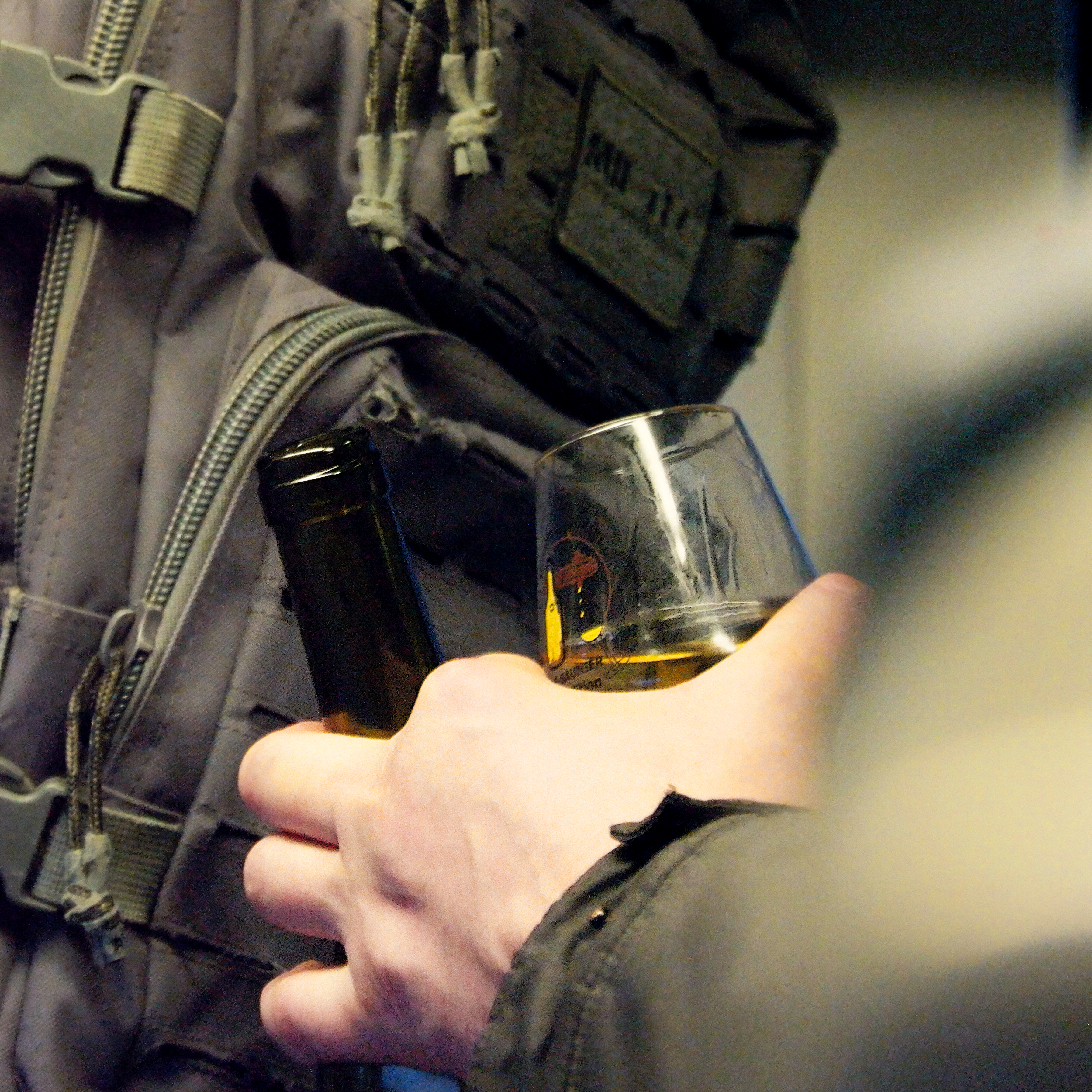 gros plan d'une main en train de tenir à la fois un verre et une bouteille de vin jaune