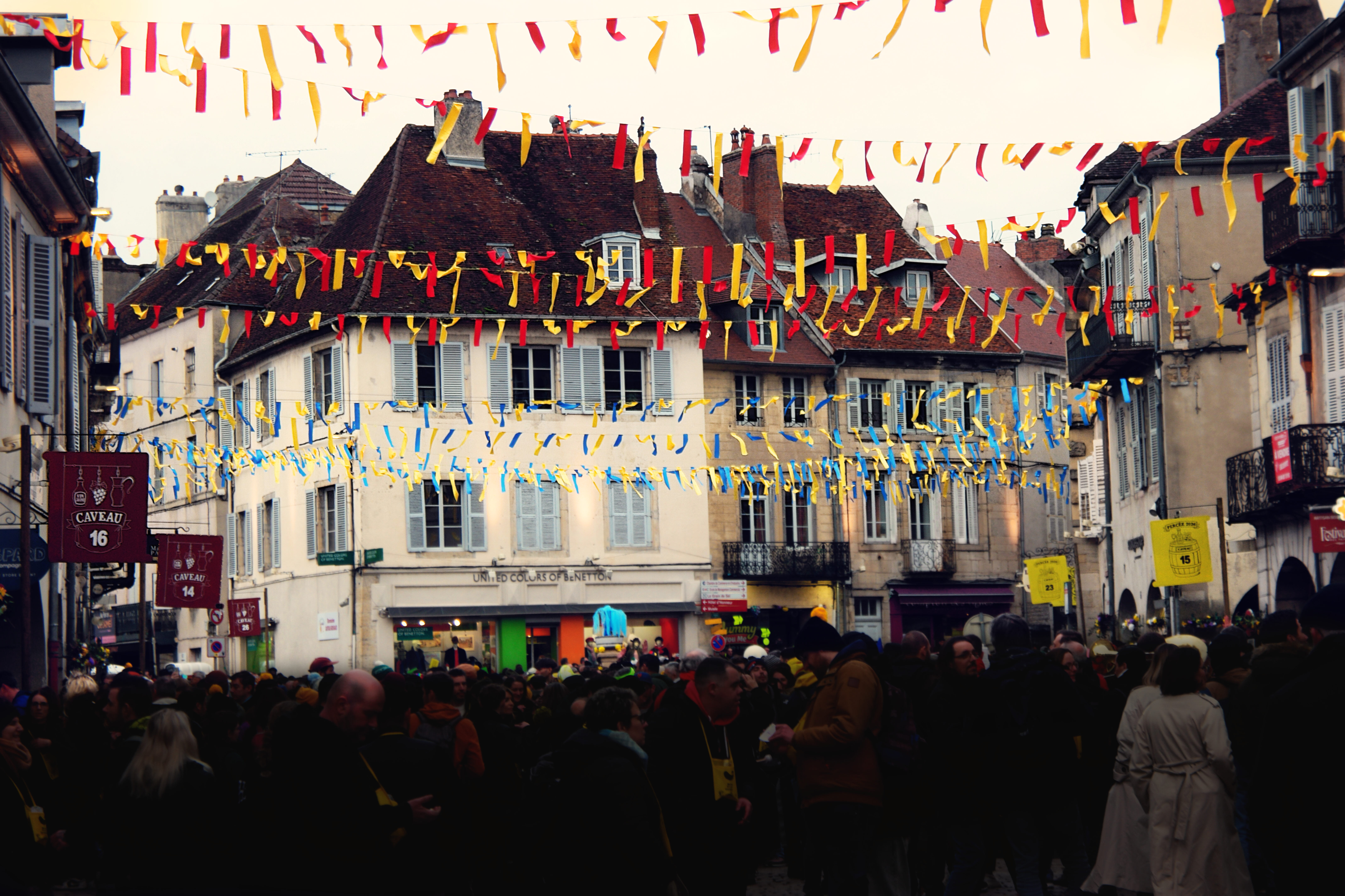 vue de la fin de la rue du commerce, noire de monde, avec des guirlandes jaune et rouge et jaune et bleue tendues de part et d'autre de la rue