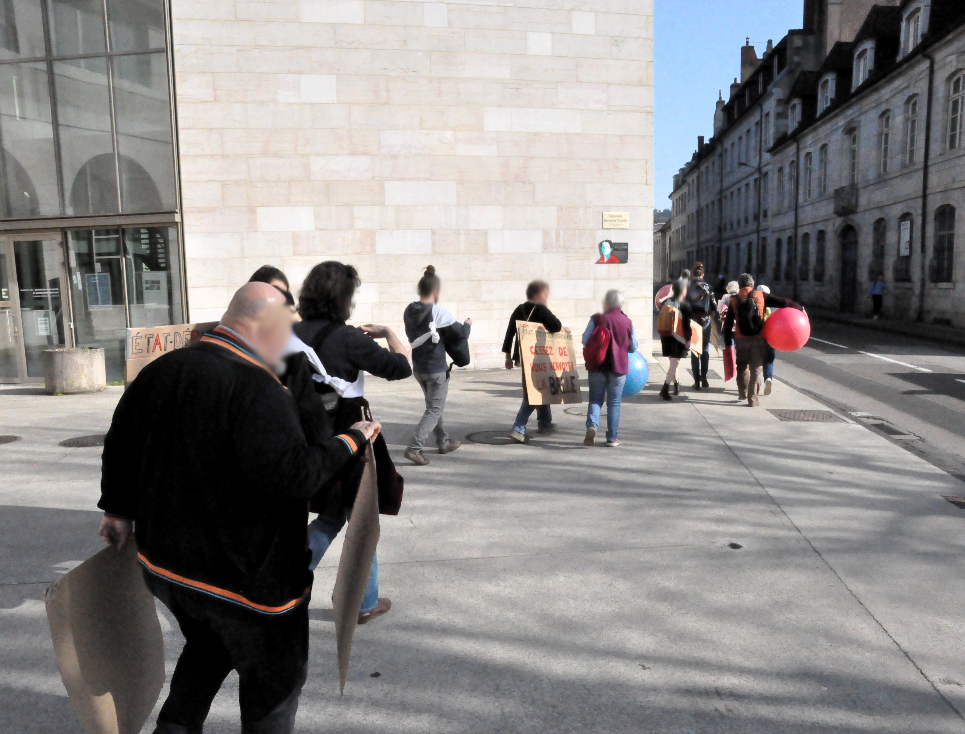 Un groupe de personnes équipées de pancartes sur le parvis de la MSHE de Besançon se dirigent vers la préfecture