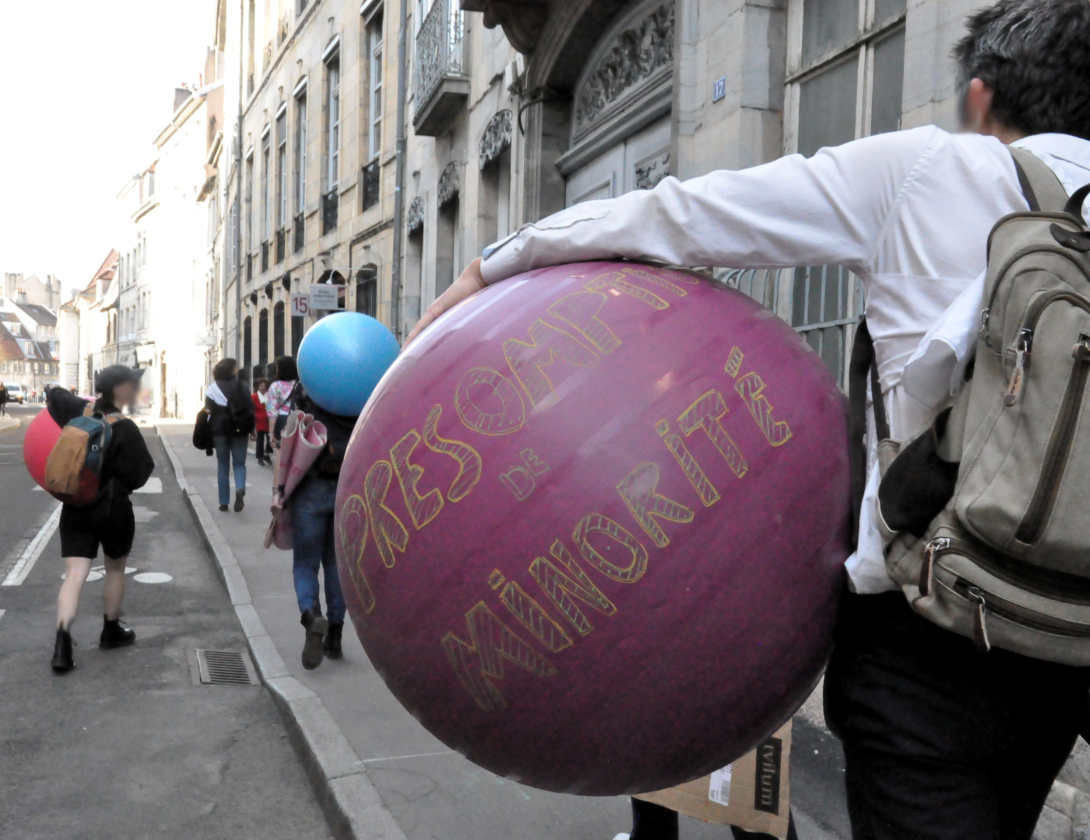Le groupe de personnes se déplace en ville, gros plan sur le ballon de gymnastique sur lequel est écrit "présomption de minorité"