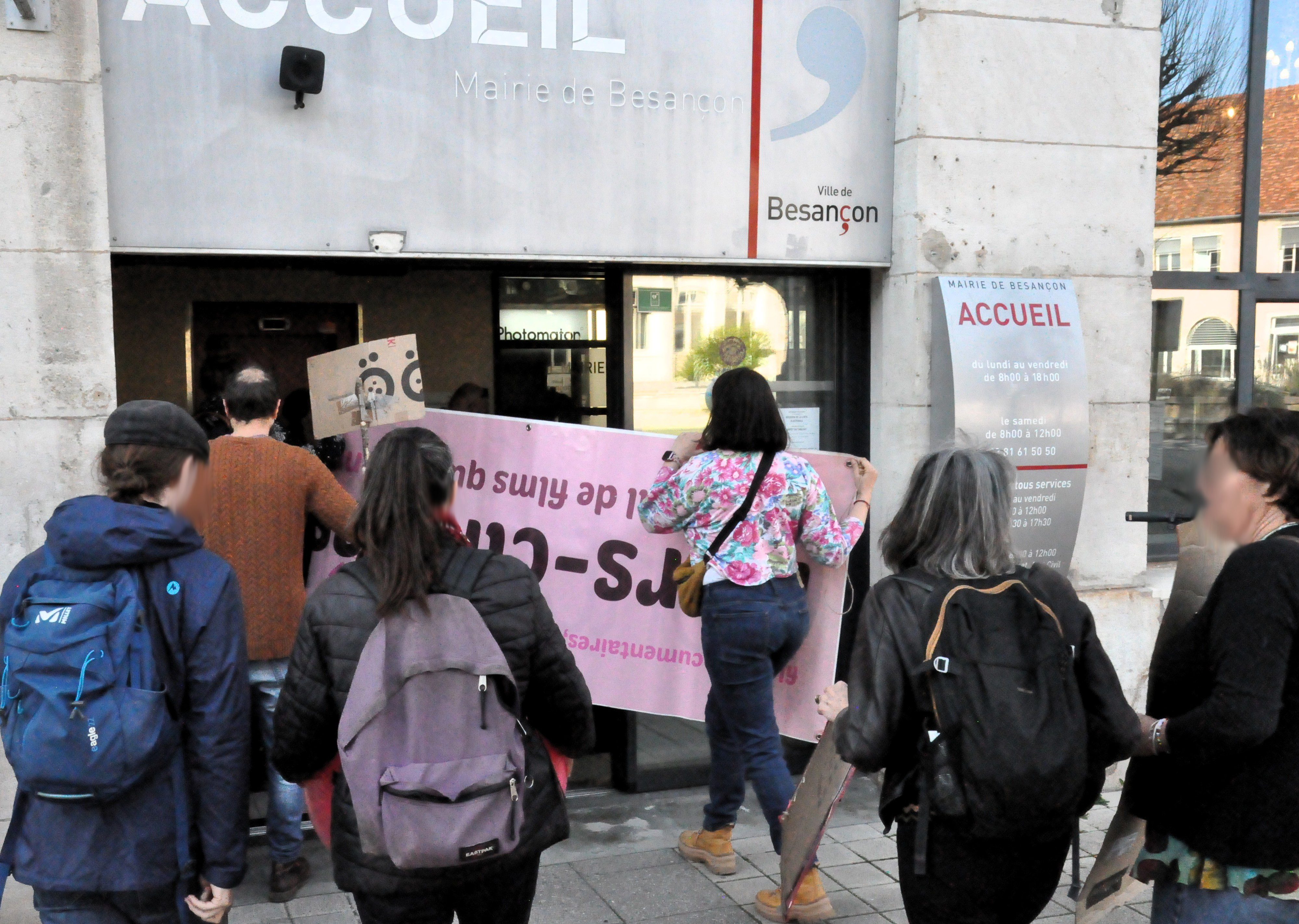 Un groupe de personnes rentrent dans les locaux de la mairie avec des pancartes.
