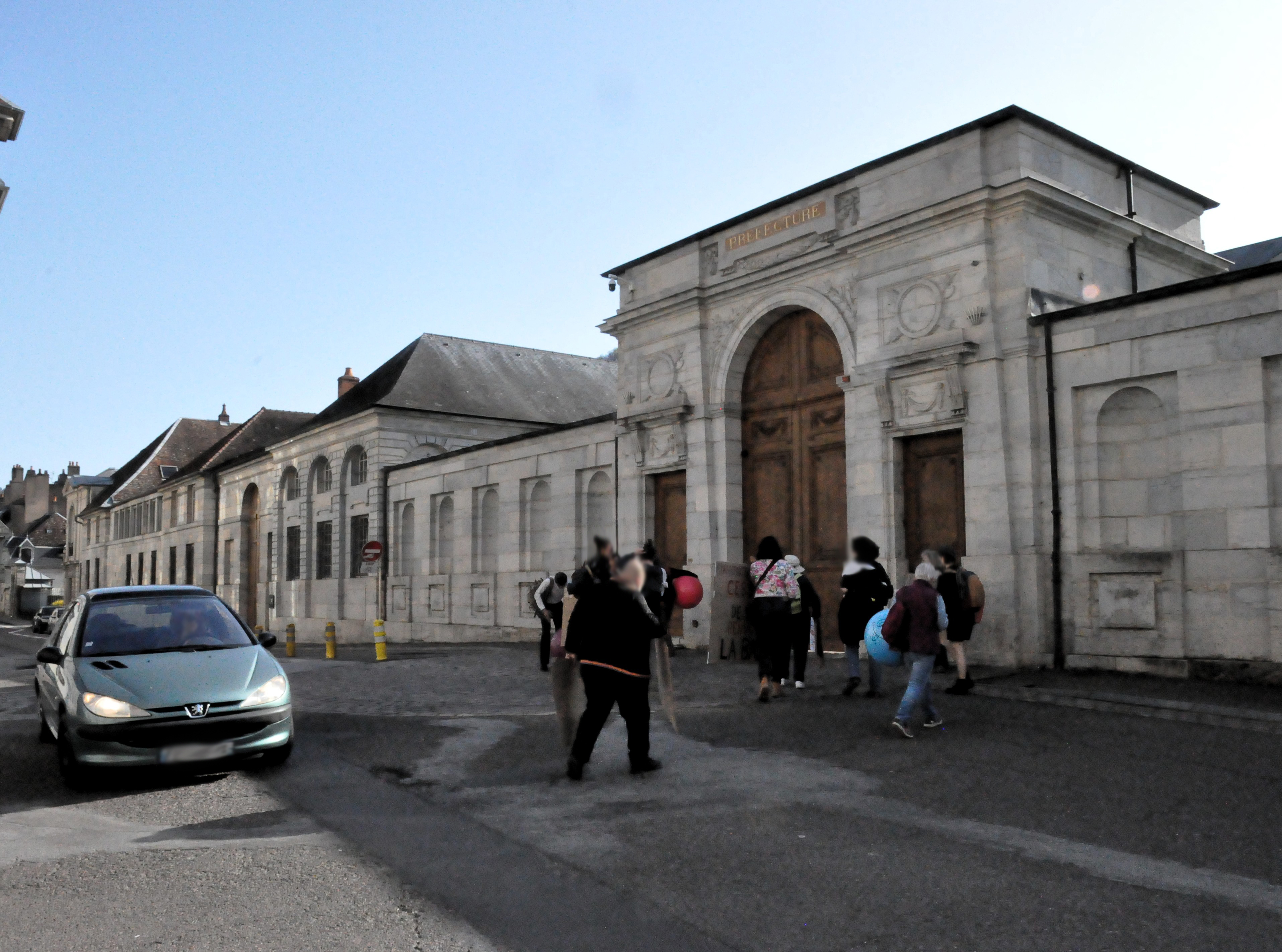 La petite dizaine de personnes, avec des pancartes et des ballons, s'installent devant la grande porte de la préfecture, à Besançon
