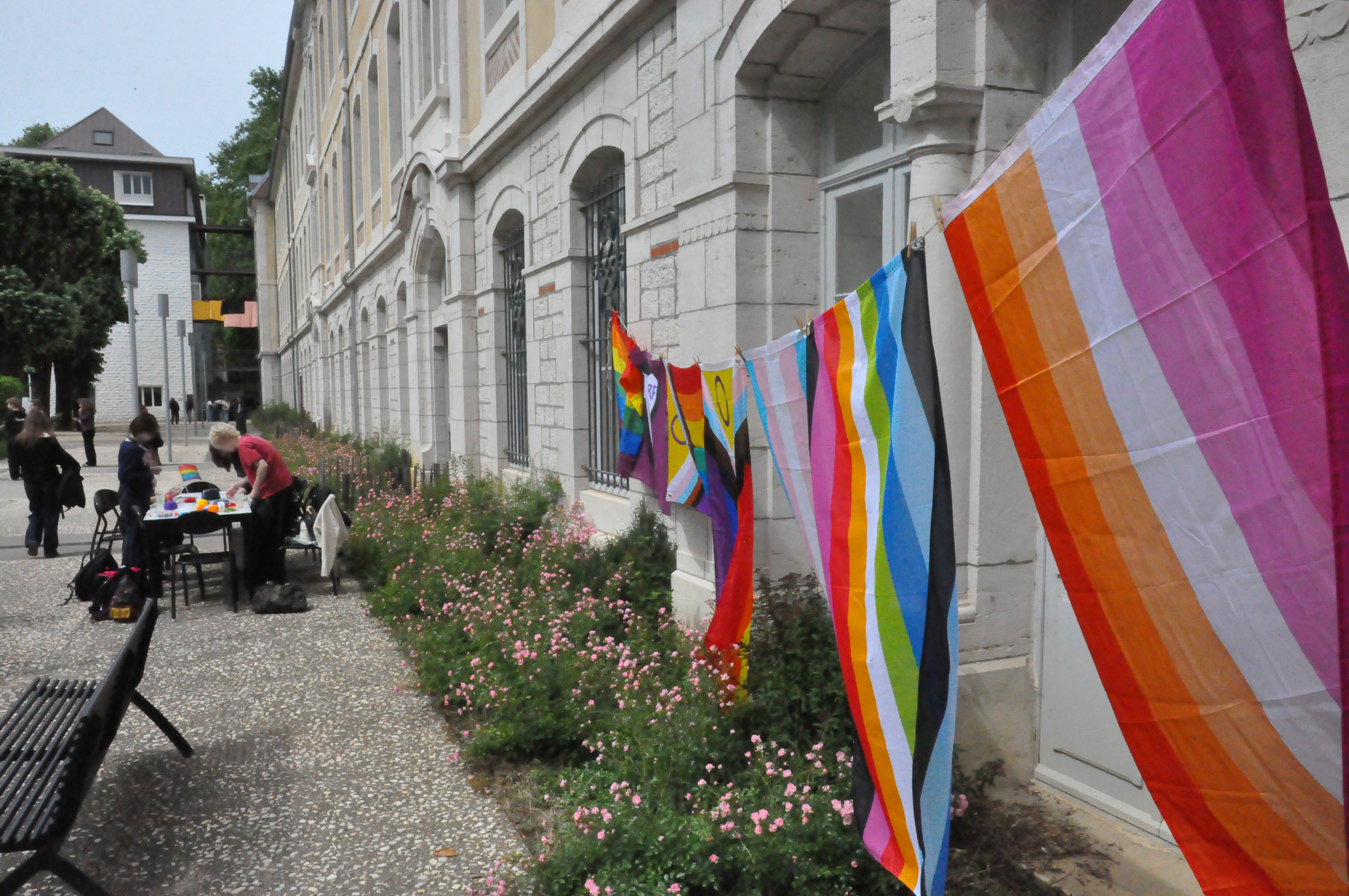 Une banderole de différents drapeaux représentants plusieurs sexualités et genre dans la cour du lycée Pasteur, au-dessus des parterres de fleur le long du mur