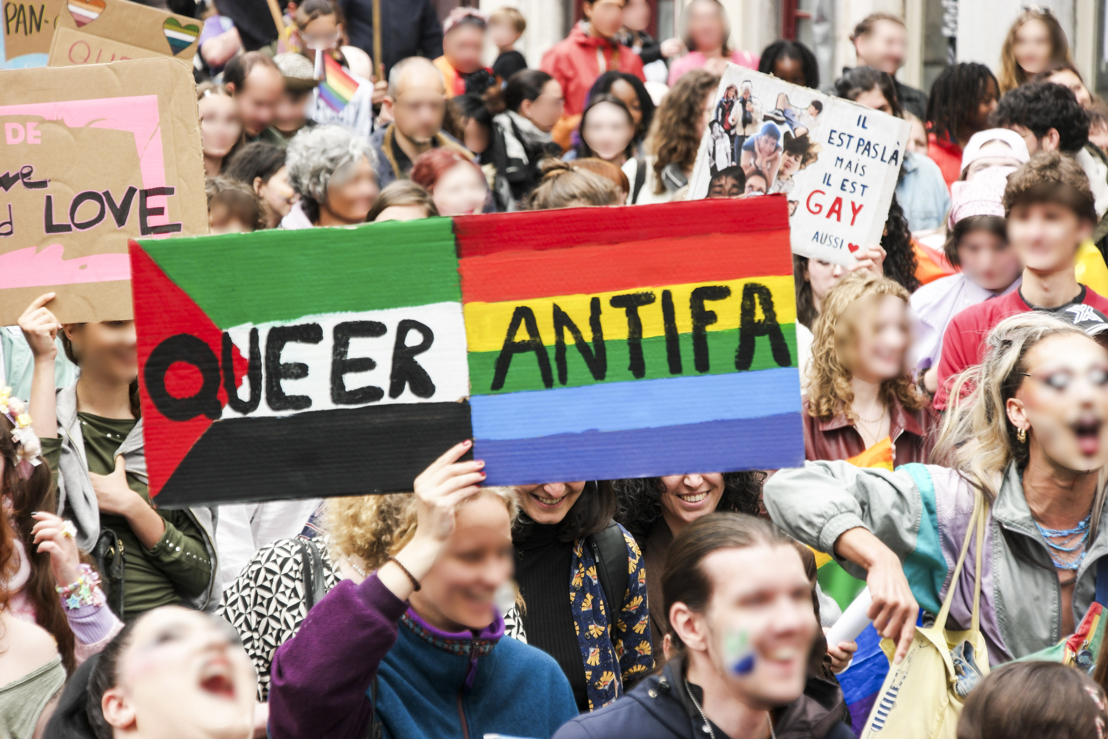 Une double pancarte dans la foule : queer (sur fond de drapeau palestinien) et antifa (sur fond de drapeau arc-en-ciel)