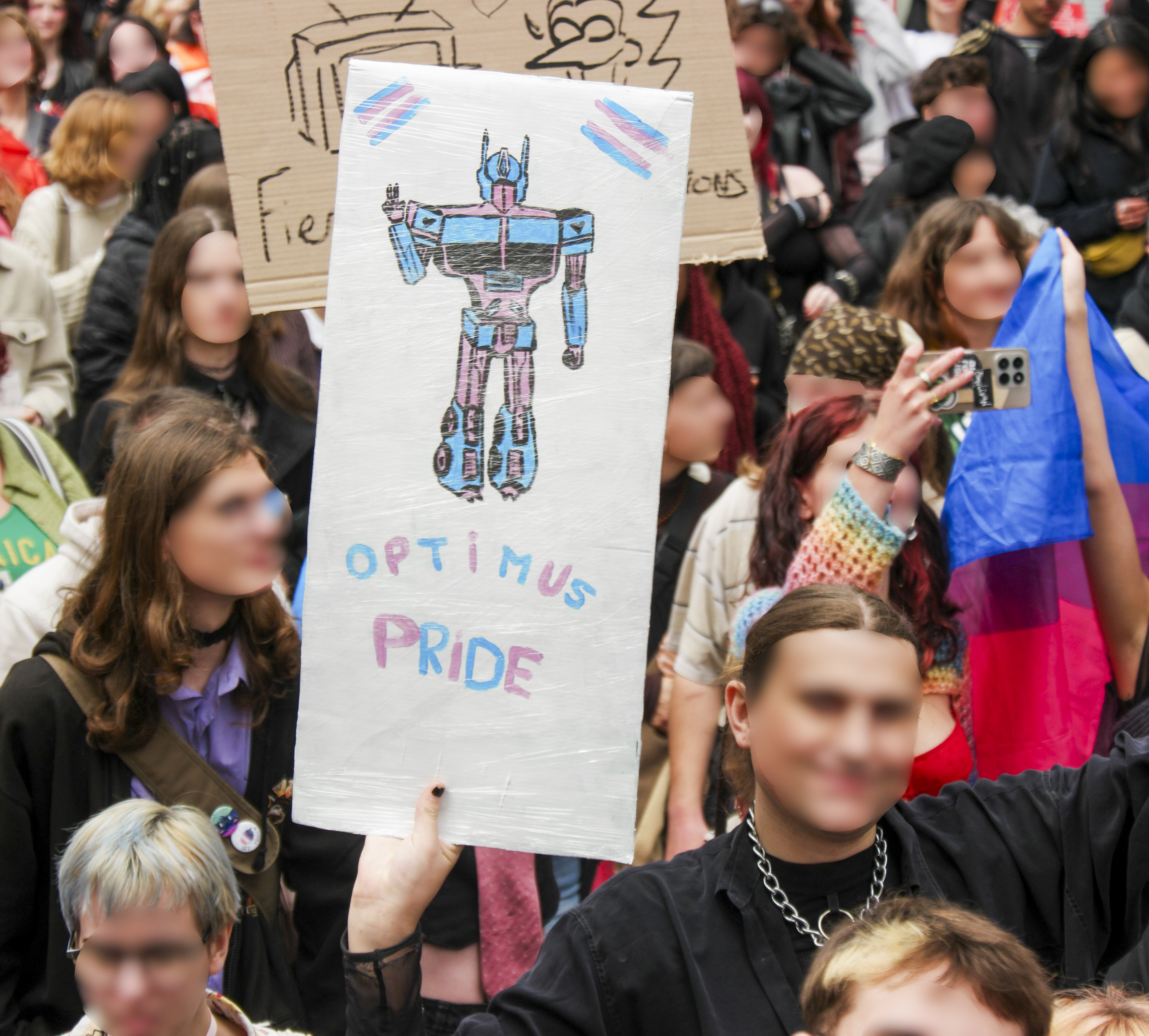 Une pancarte Optimus Pride, avec le dessin du robot transformer aux couleurs trans