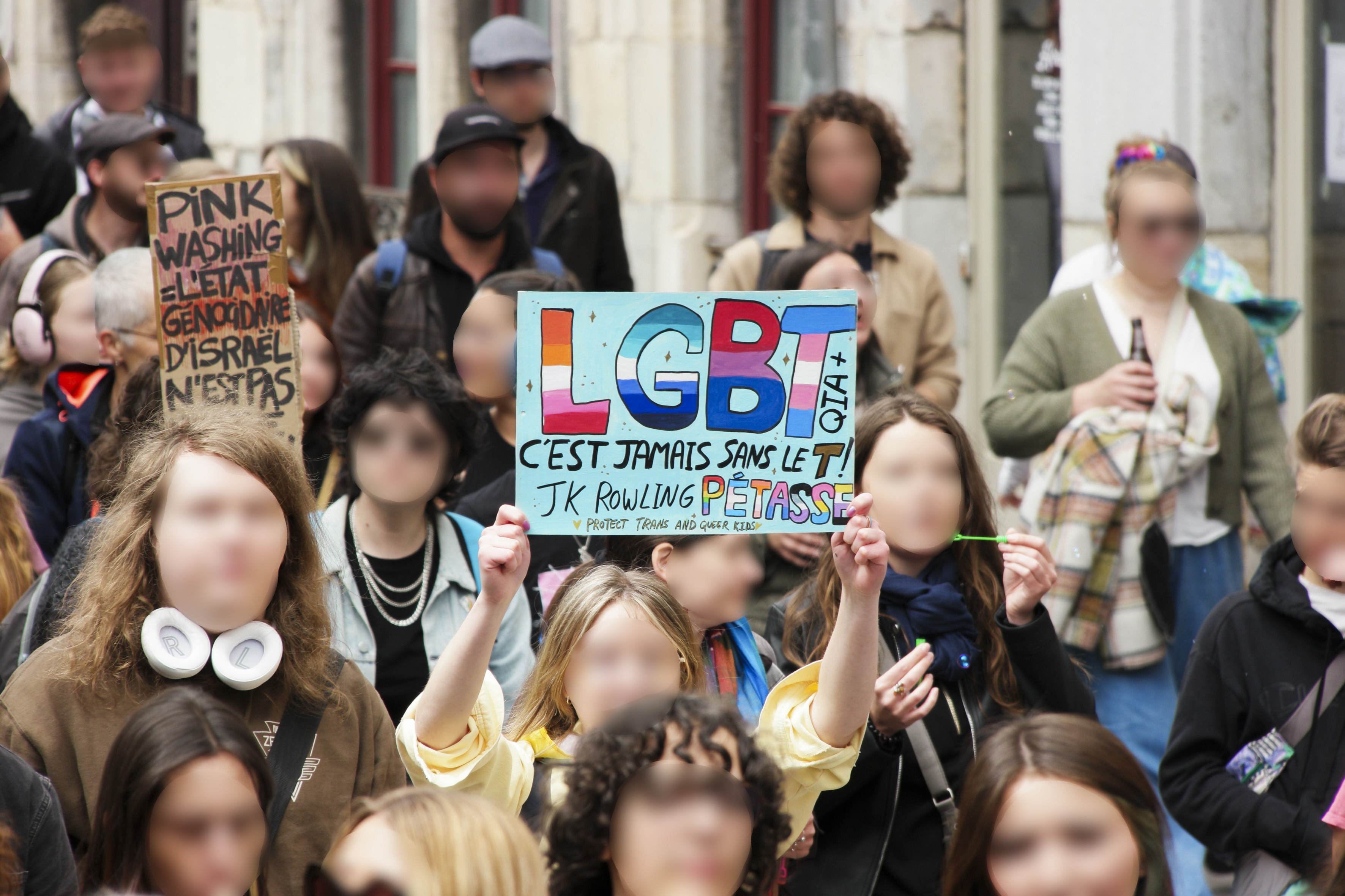 deux pancartes : pink washing, l'état génocidaire d'Israël n'est pas (probablement "un allié", mais la pancarte est masquée par une tête.
L'autre pancarte : LGBT jamais sans le T. JK Rowling pétasse !