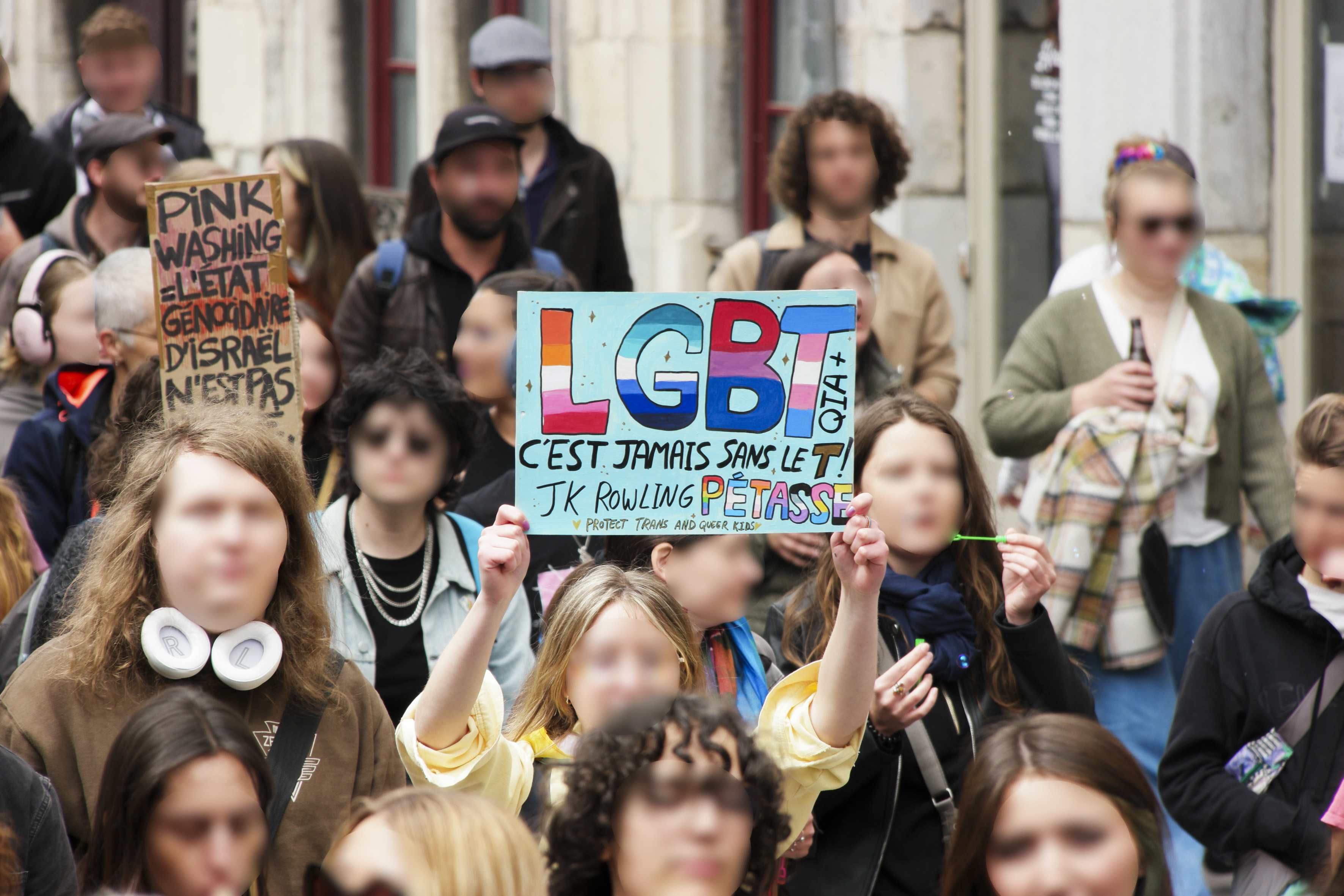 deux pancartes : pink washing, l'état génocidaire d'Israël n'est pas (probablement "un allié", mais la pancarte est masquée par une tête.
L'autre pancarte : LGBT jamais sans le T. JK Rowling pétasse !