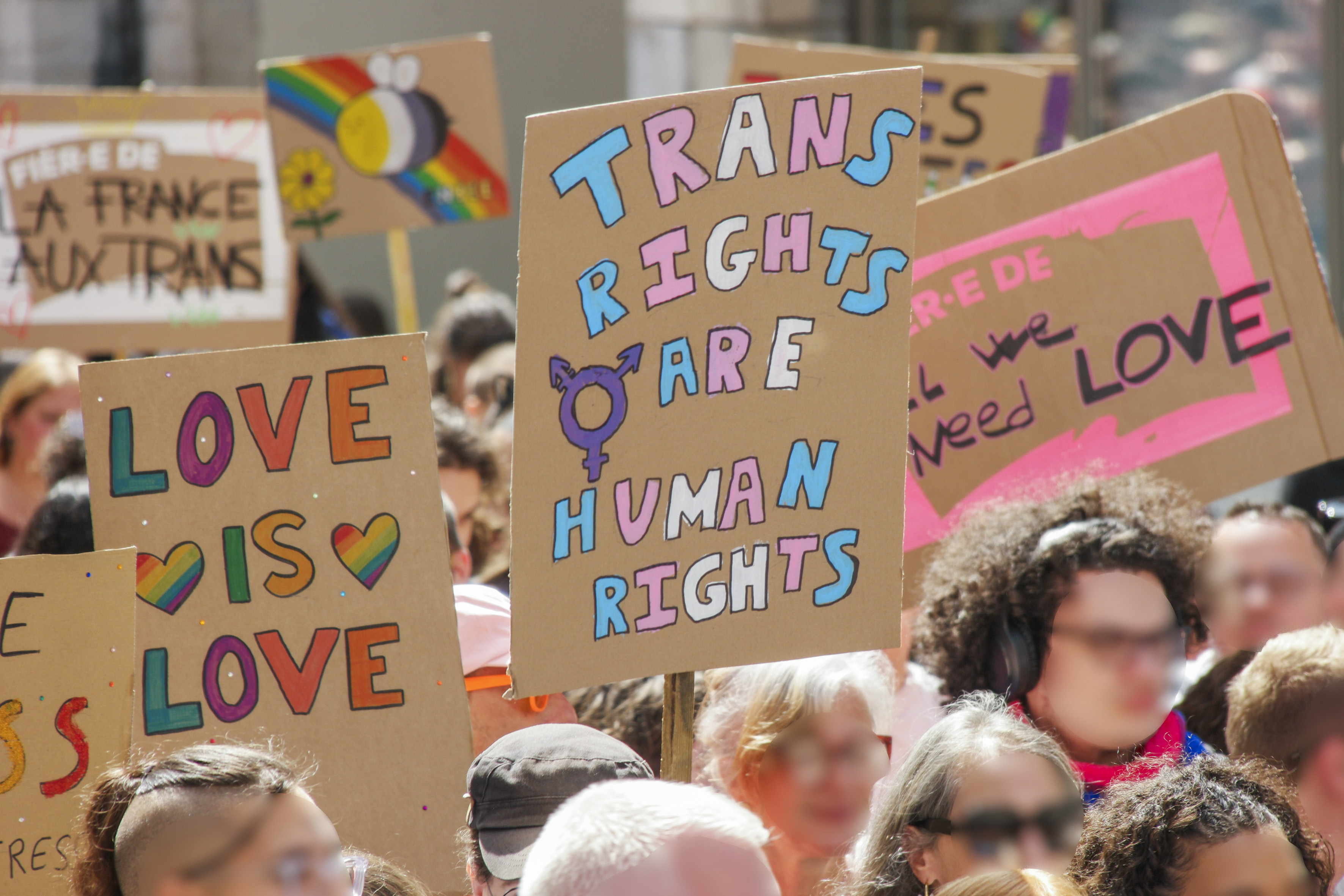 Foule de laquelle se distinguent quatre pancartes : la France aux trans, trans rights are humans rights, all we need is love, love is love