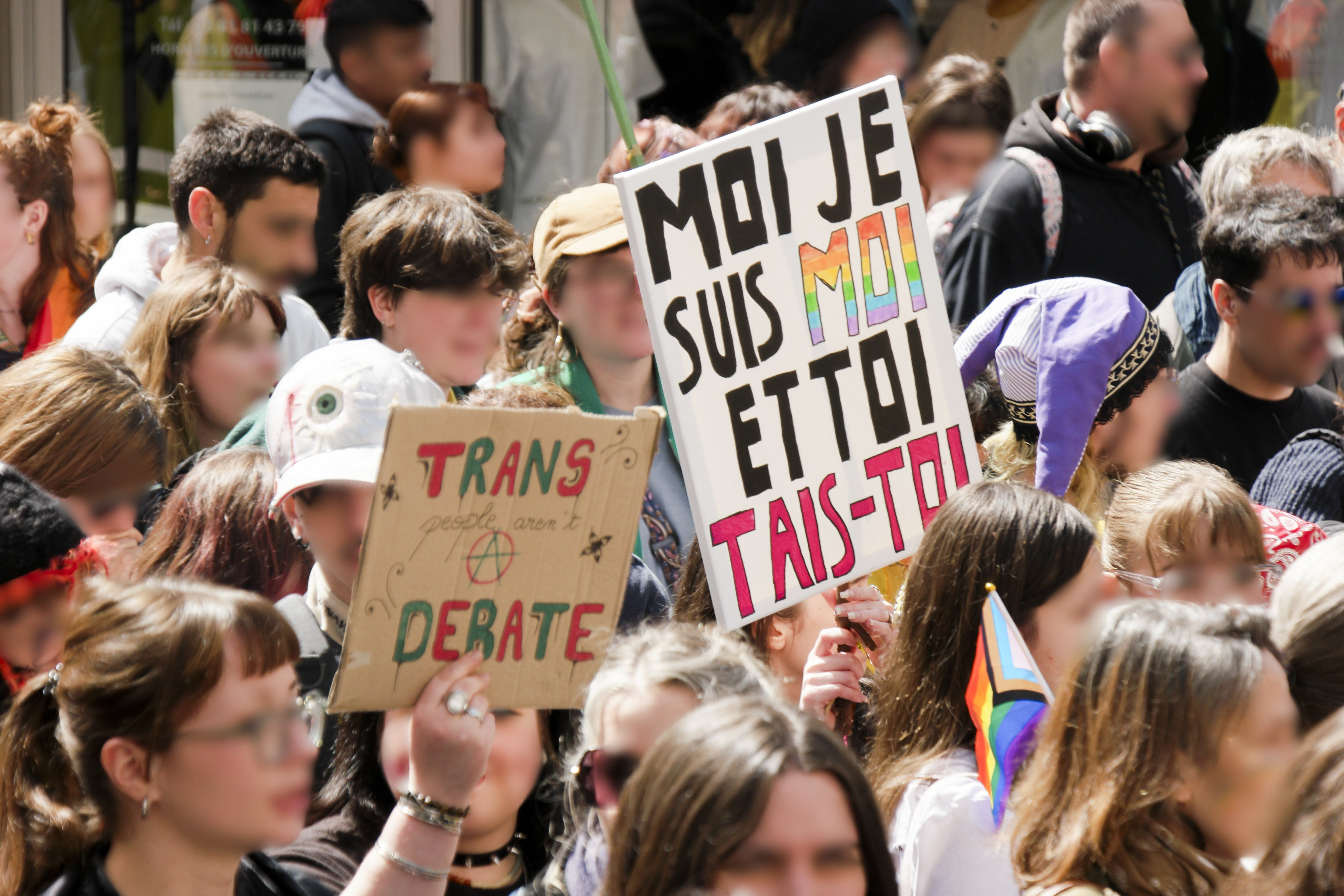 Deux pancartes dans la foule : Trans people aren't a debate (avec un A anarchiste) et un autre : moi je suis moi et toi tais-toi