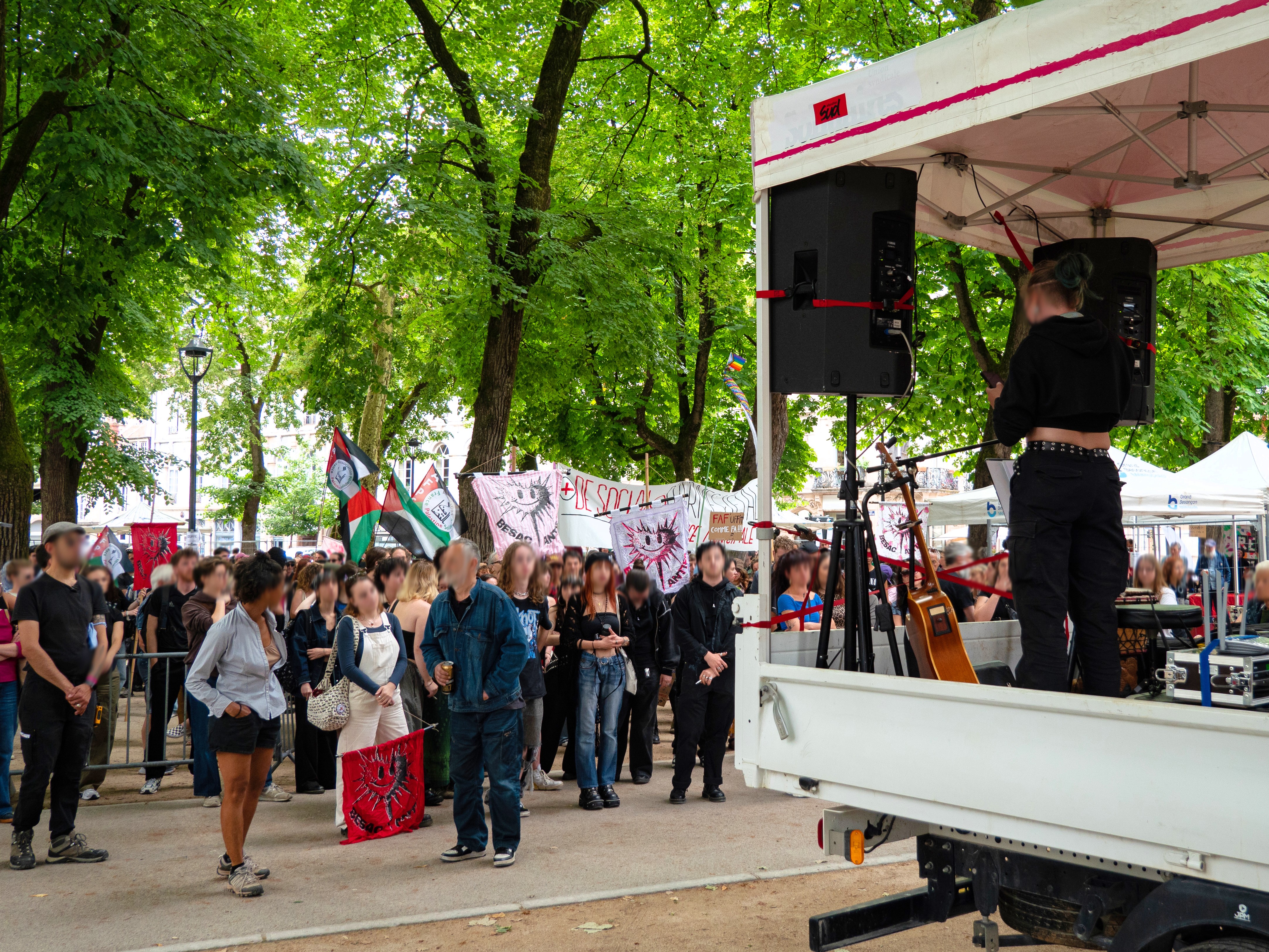 Prise de parole depuis le camion de la sono devant une foule de gens, avec de nombreux drapeaux du BAF, promenade Granvelle