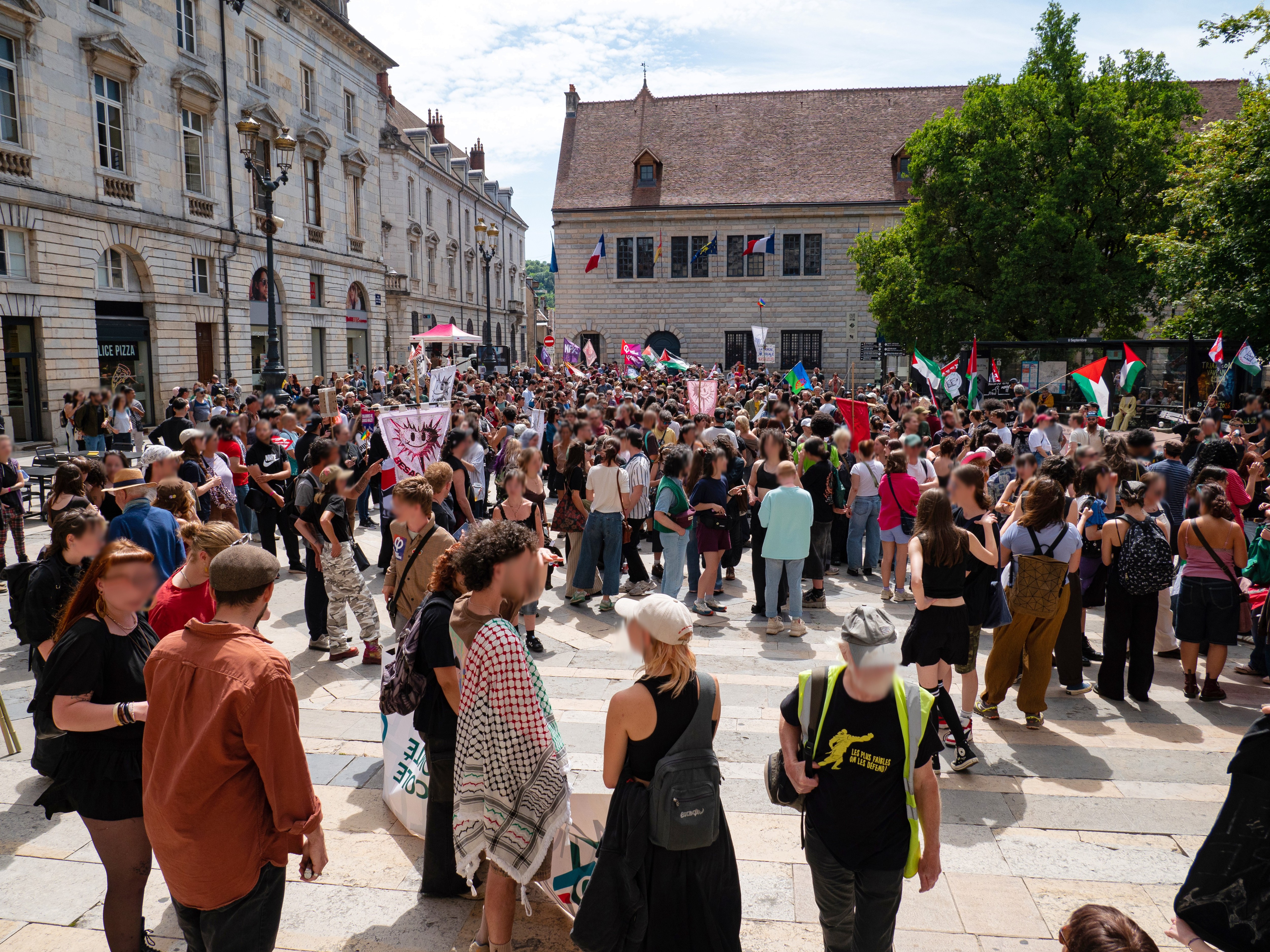 La place du Huit-Septembre noire de monde pendant le défilé, avec de nombreux drapeaux : le BAF, de Palestine, du NPA, de la France Insoumise ou encore de la fierté gitane,