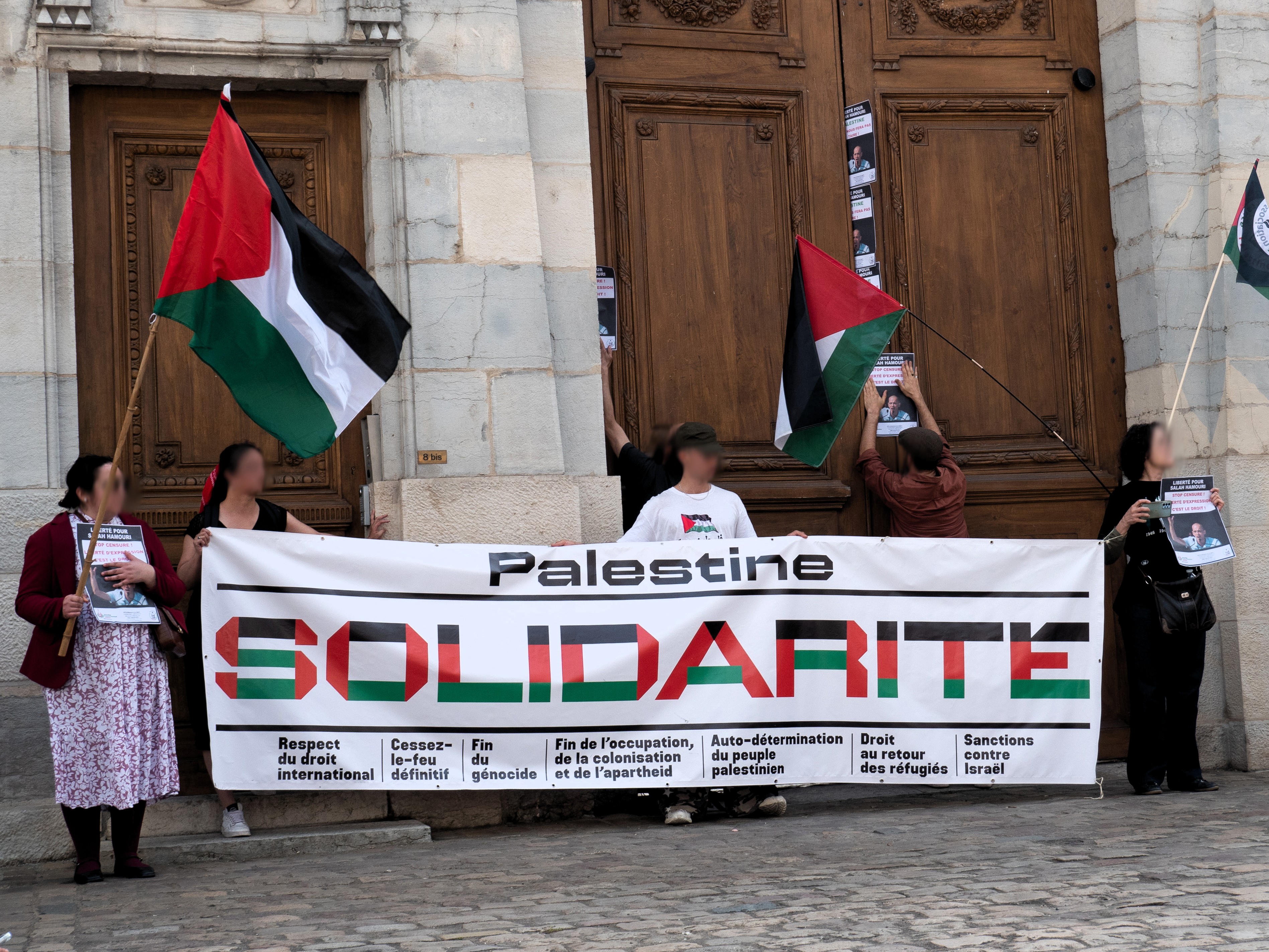 Des militant·es déploient une banderole Palestine Solidarité et des drapeaux palestiniens devant la porte de la préfecture pour dénoncer la censure de l'avocat franco-palestinien Salah Hamouri