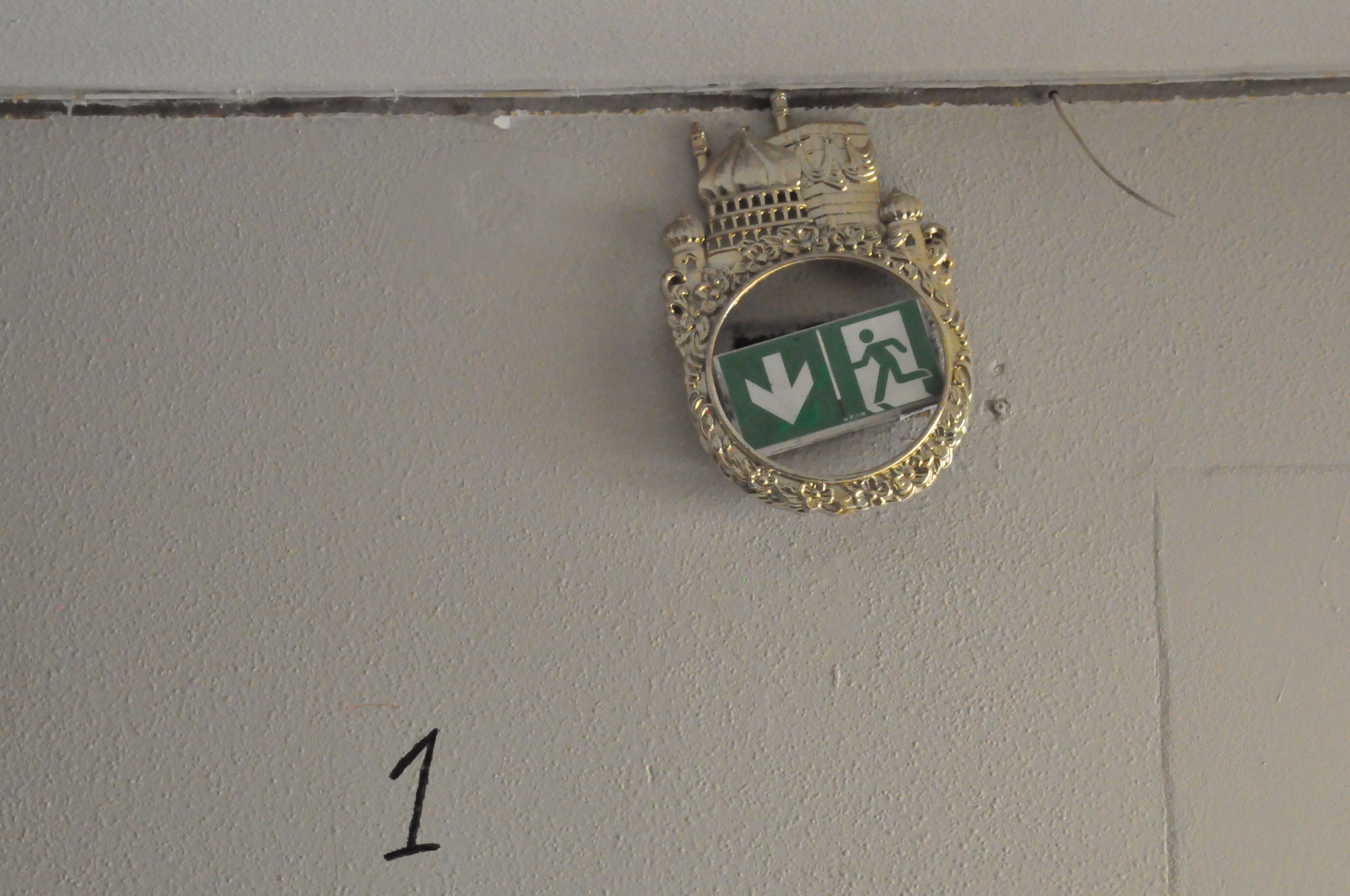 un logo d'issue de secours, entouré d'une pièce en métal doré représentant une mosquée, abandonnée