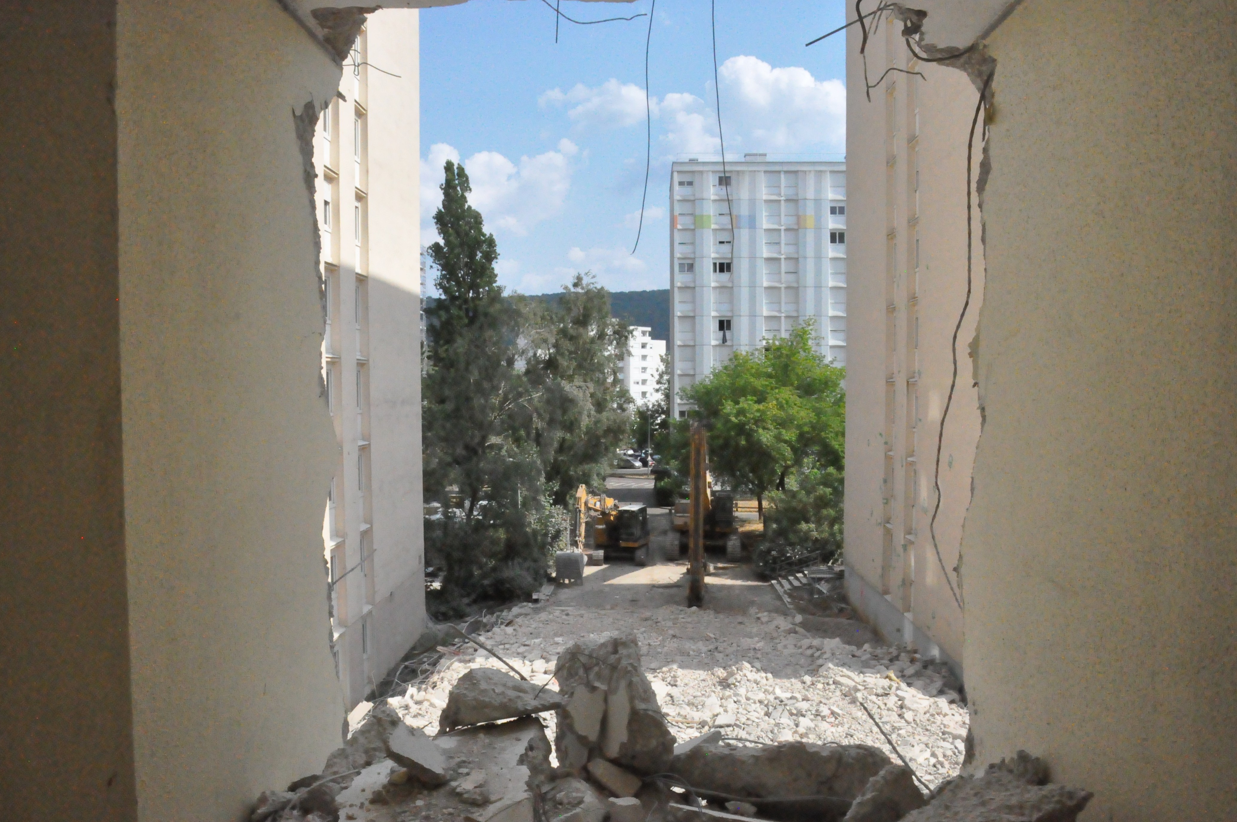 vue sur les pelleteuses extérieures depuis l'intérieur, via un mur tombé dont il ne reste qu'un tas de gravats au milieu du chemin