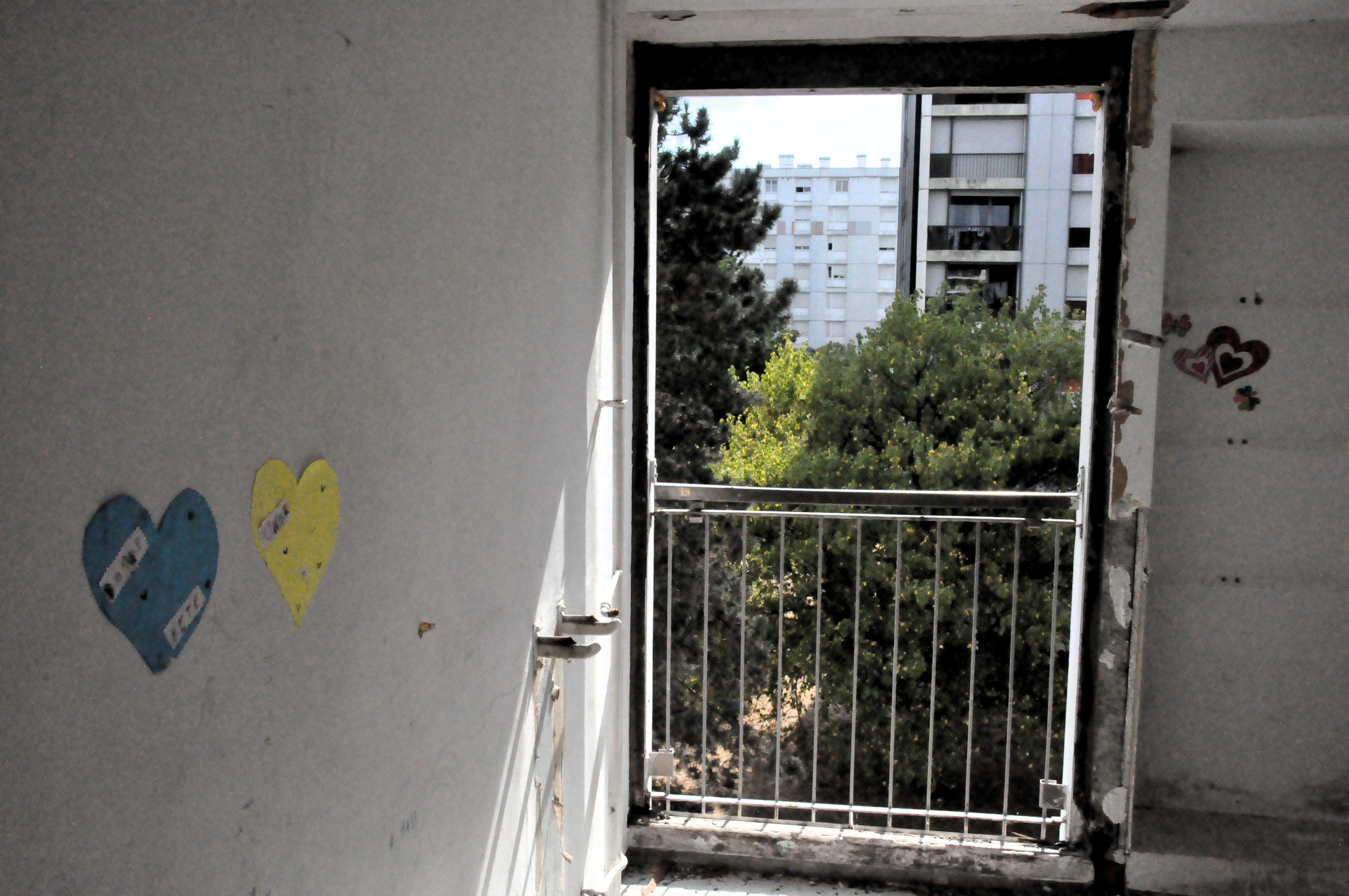 une porte vitrée arrachée dans une petite pièce délabrée, dont on voit toujours des petits ornements en cœur appliqués par les anciens locataires