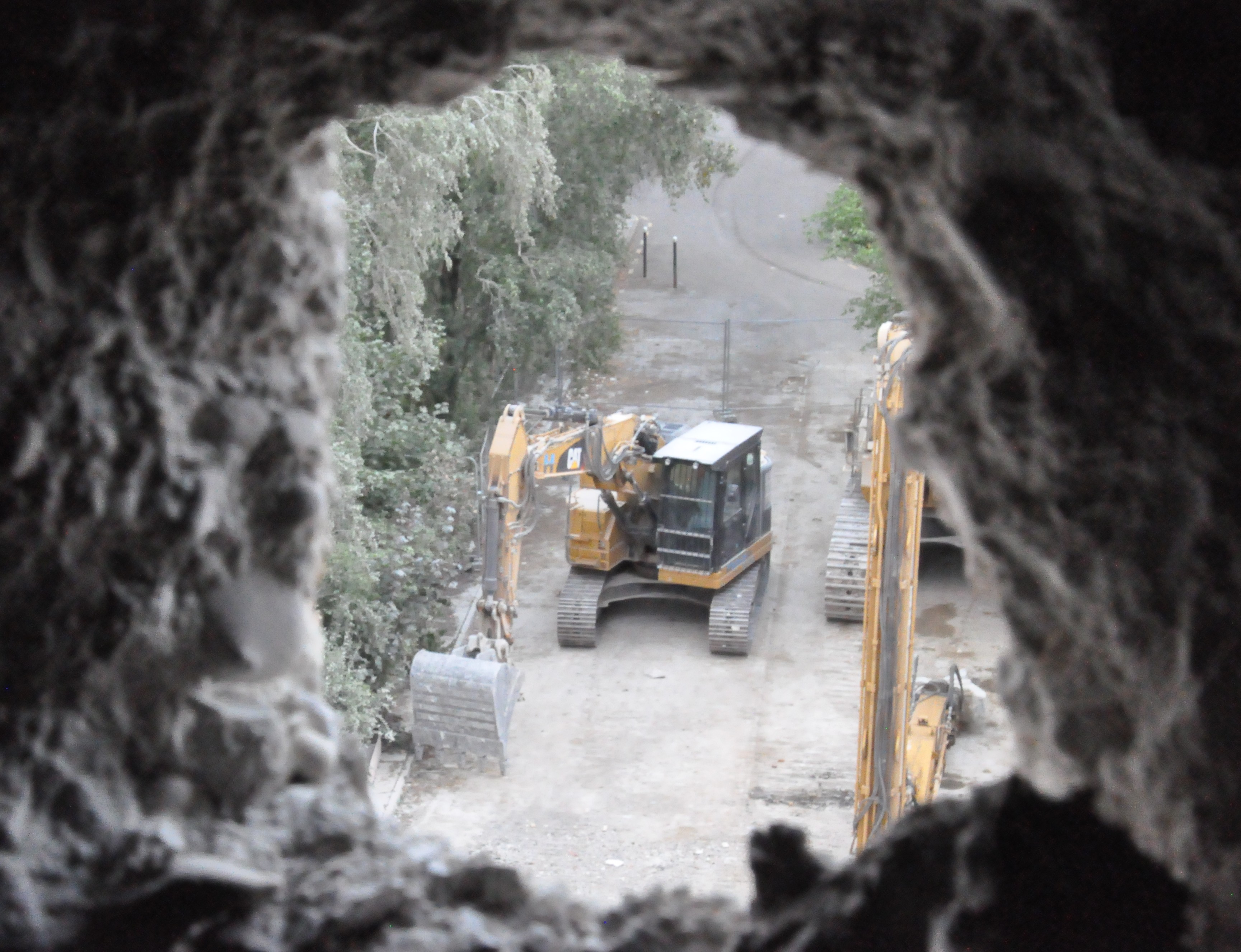 vue sur une pelleteuse en contrebas depuis un trou dans un mur