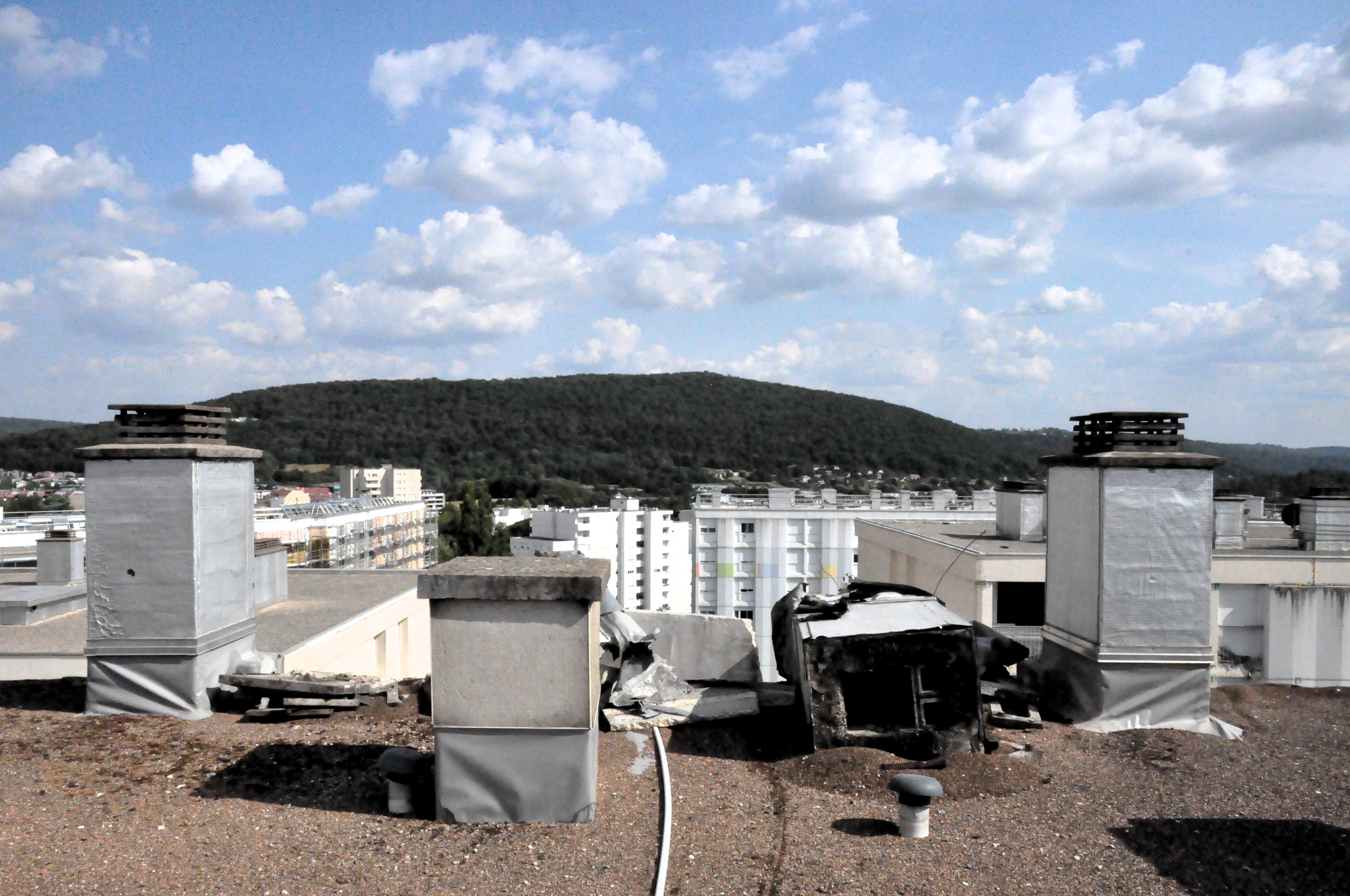 vue des toits avec les cheminées en béton, dont une est renversée sur le flanc. À l'arrière-plan, des barres d'immeuble