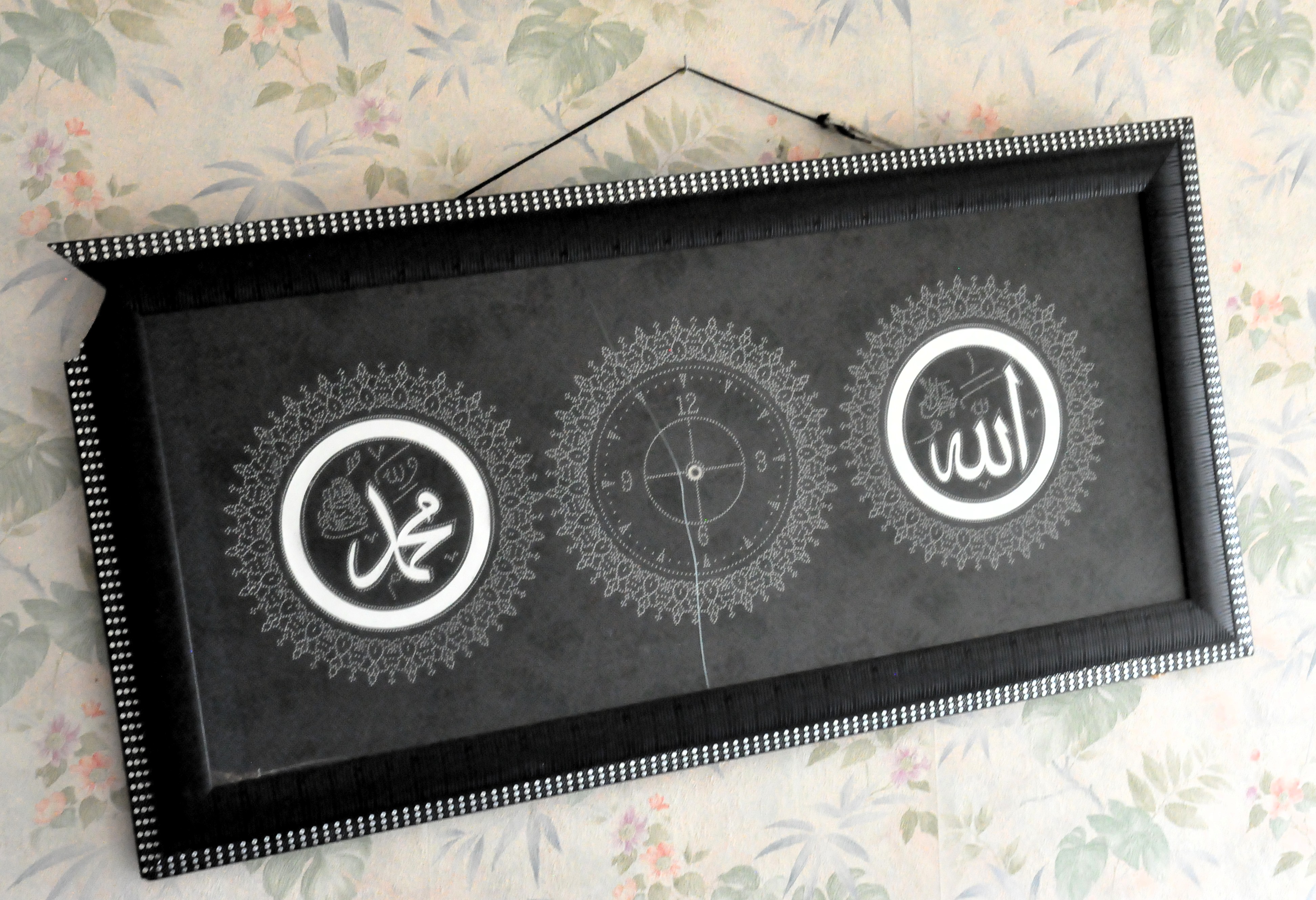 un cadre légèrement ébréché et tordu, représentant trois cercles, un central avec une horloge, deux latéraux comportant des écritures arabes