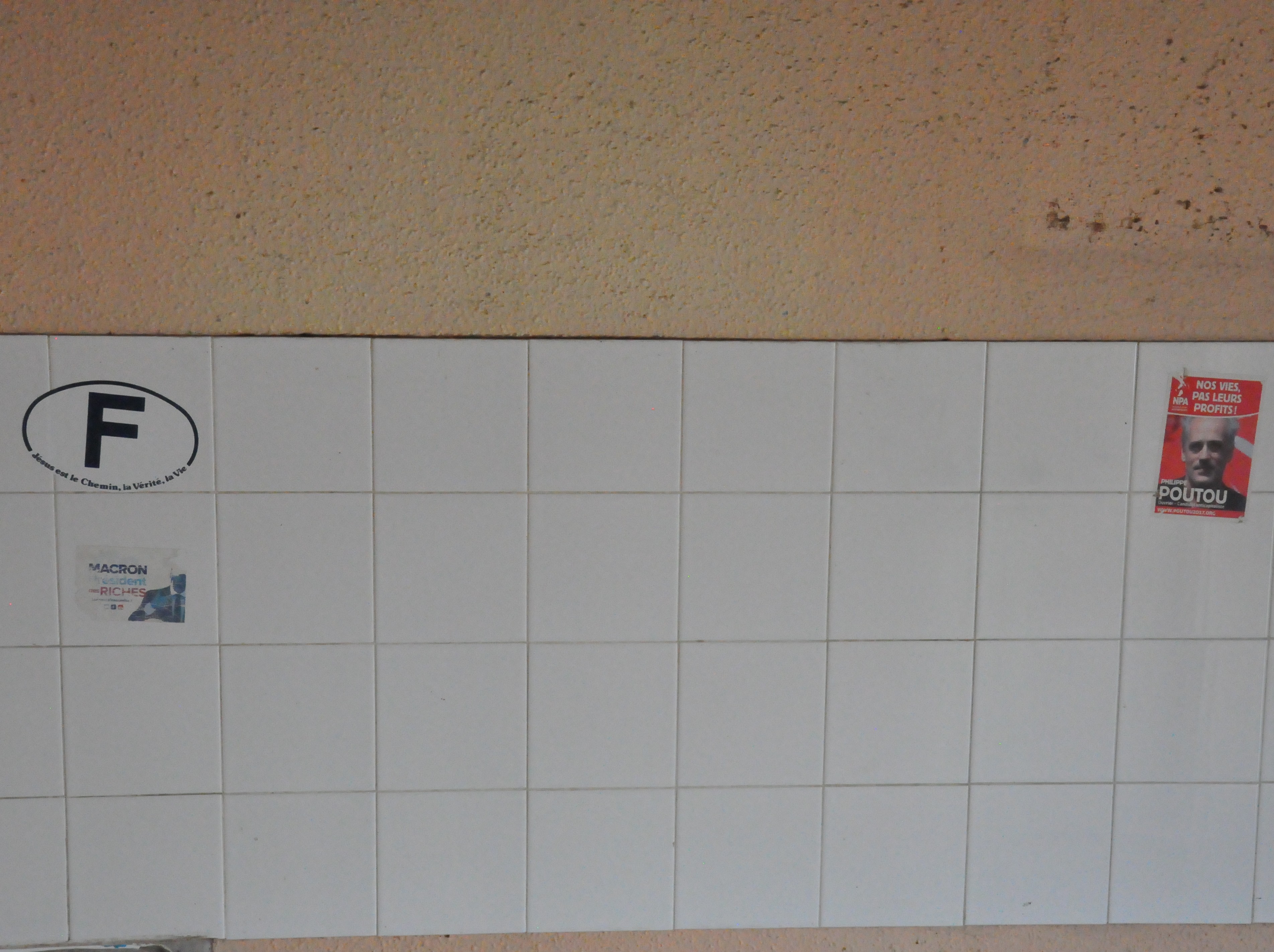 carrelage de cuisine, blanc, vide, à l'exception de trois stickers sur les côtés : Jésus est le chemin, la vie, la vérité, autour du logo F des véhicules français, un autre Macron président des riches, et un dernier représentant Philippe Poutou, du NPA : nos vies, pas leurs profits