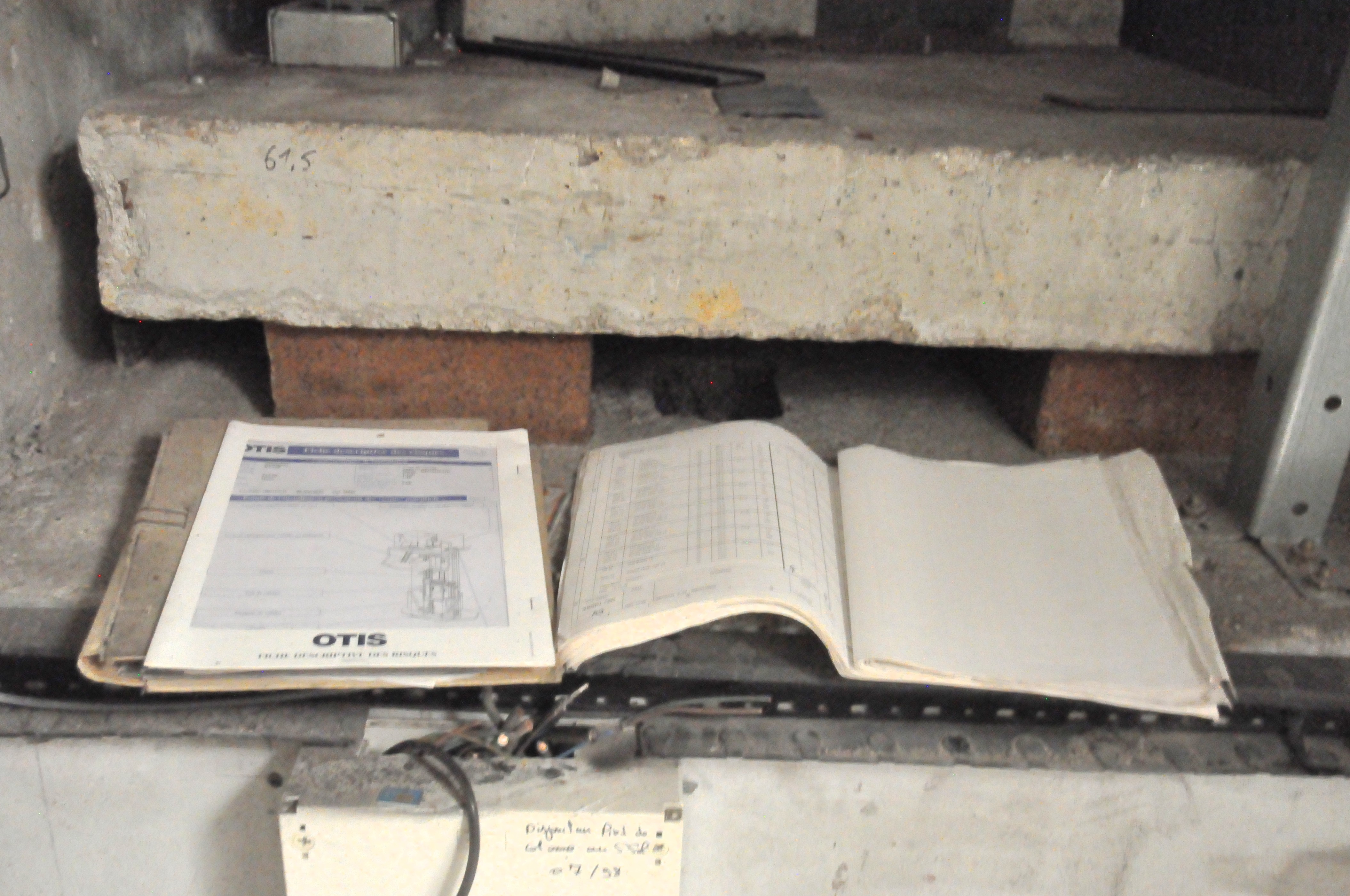 des carnets d'entretien et une notice d'ascenseur laissés à l'abandon à côté d'un mur électrifié