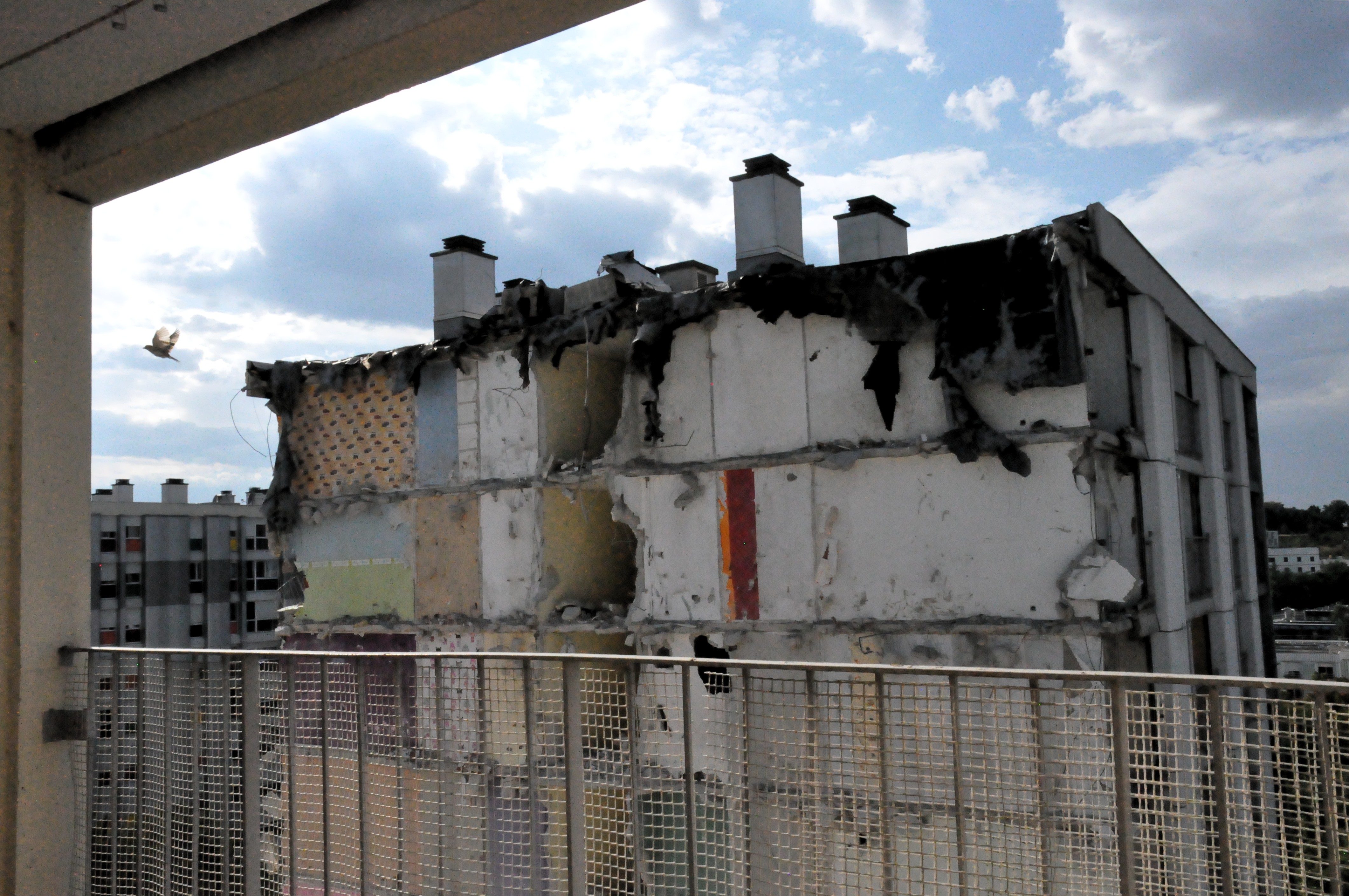 vue depuis un balcon désaffecté la façade d'un immeuble totalement arrachée. Un oiseau s'envole dans le coin de l'image