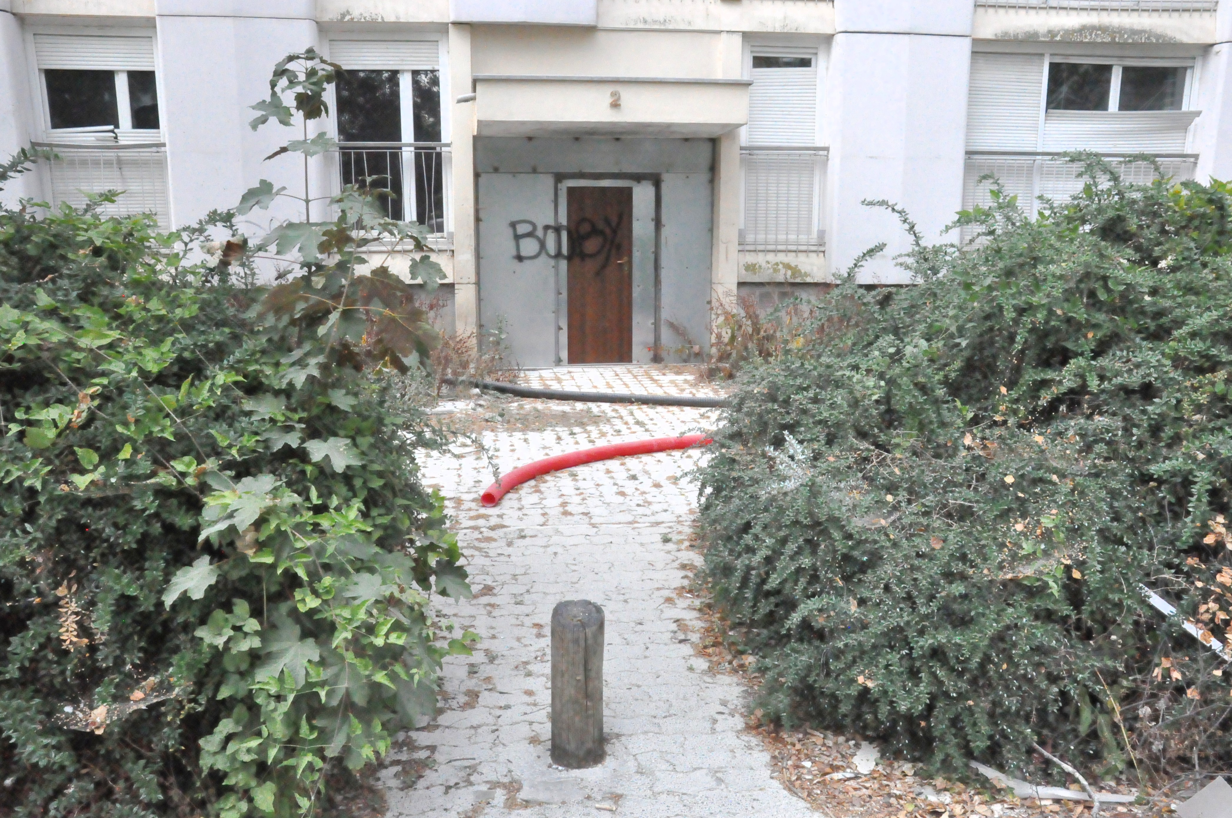 entrée d'immeuble désaffectée, avec deux tuyaux posés là, et un tag boobx sur la porte. On y accède en passant entre deux buissons laissés en friche