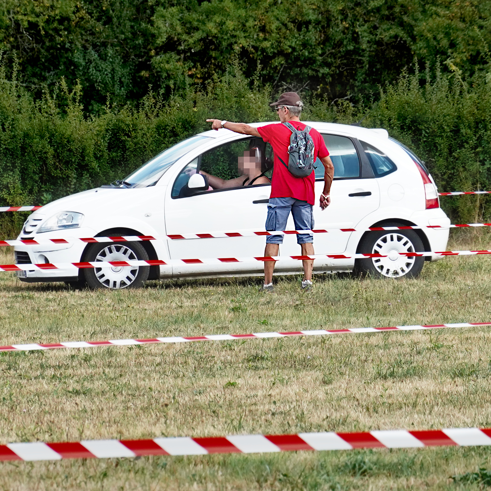 Une personne en t-shirt rouge indique à une conductrice dans sa voiture où garer sa voiture