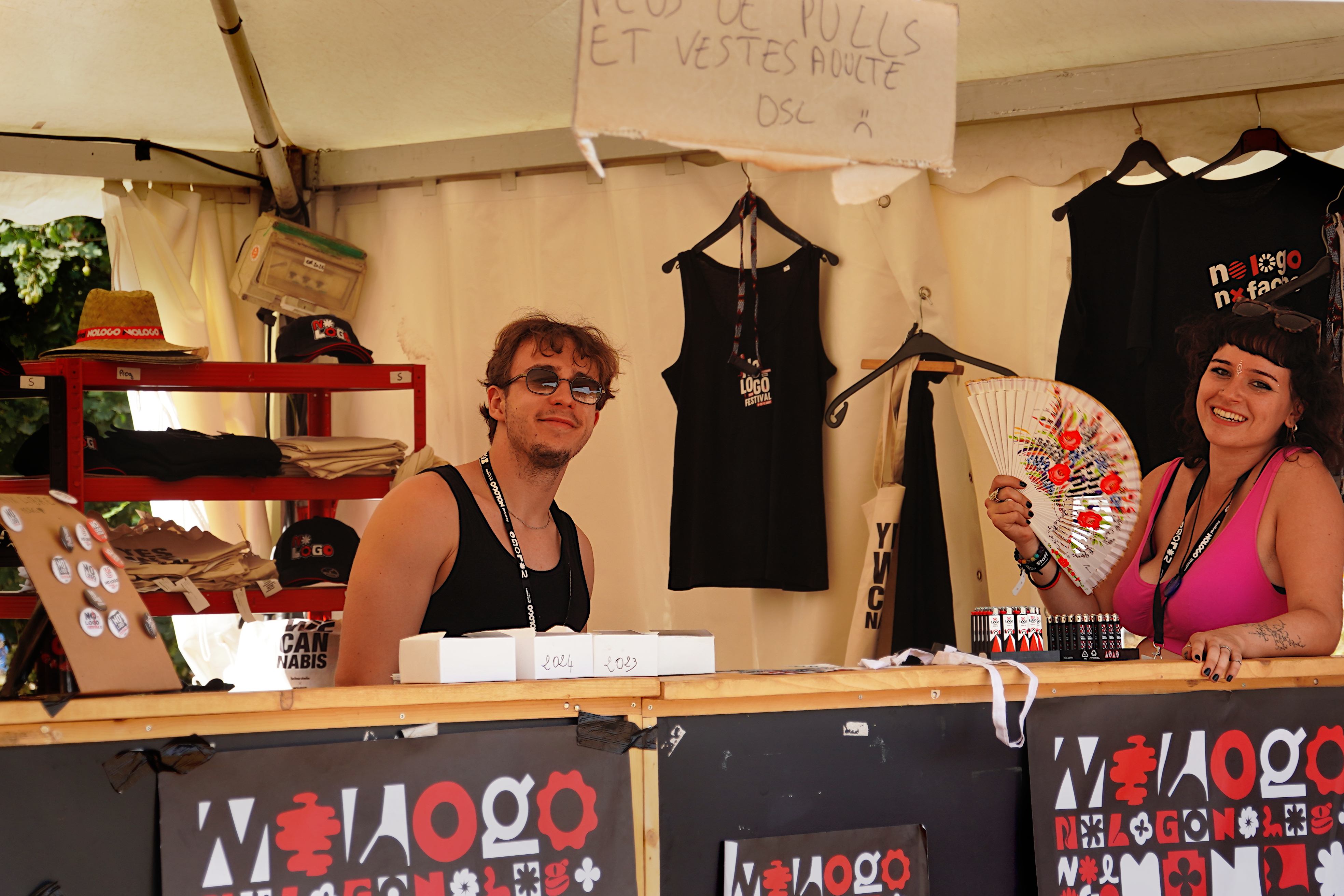 Photo d'un stand de merchandising aux couleurs du No Logo, tenu par deux personnes qui prennent la pose souriante pour le cliché
