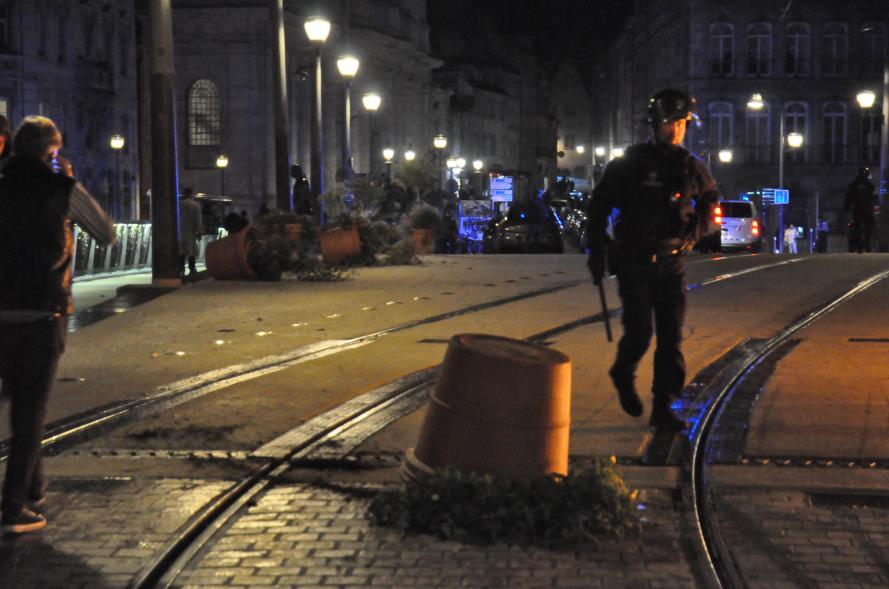Des pots de palmiers et de fleurs retournées sur le pont Battant, un policier matraque à la main avance