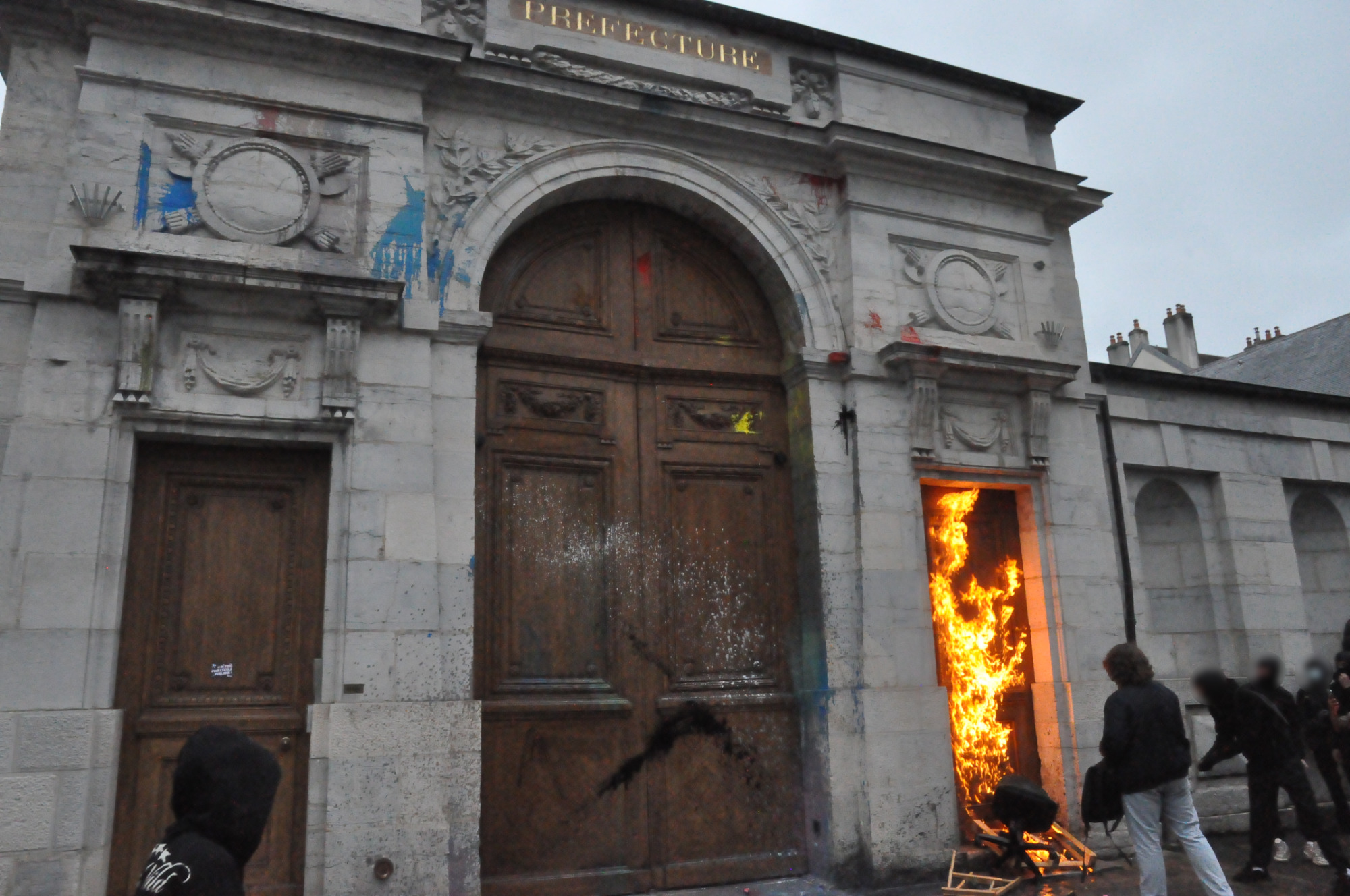 La porte de la préfecture parsemée de d'éclats de peinture, devant la petite porte à droite un départ de feu commence
